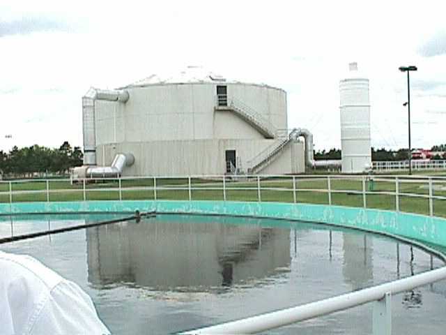 Exterior of a water treatment facility with a large cylindrical tank and circular settling basin.
