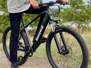 A person holding the handlebars of a dark electric mountain bike on a dirt path.