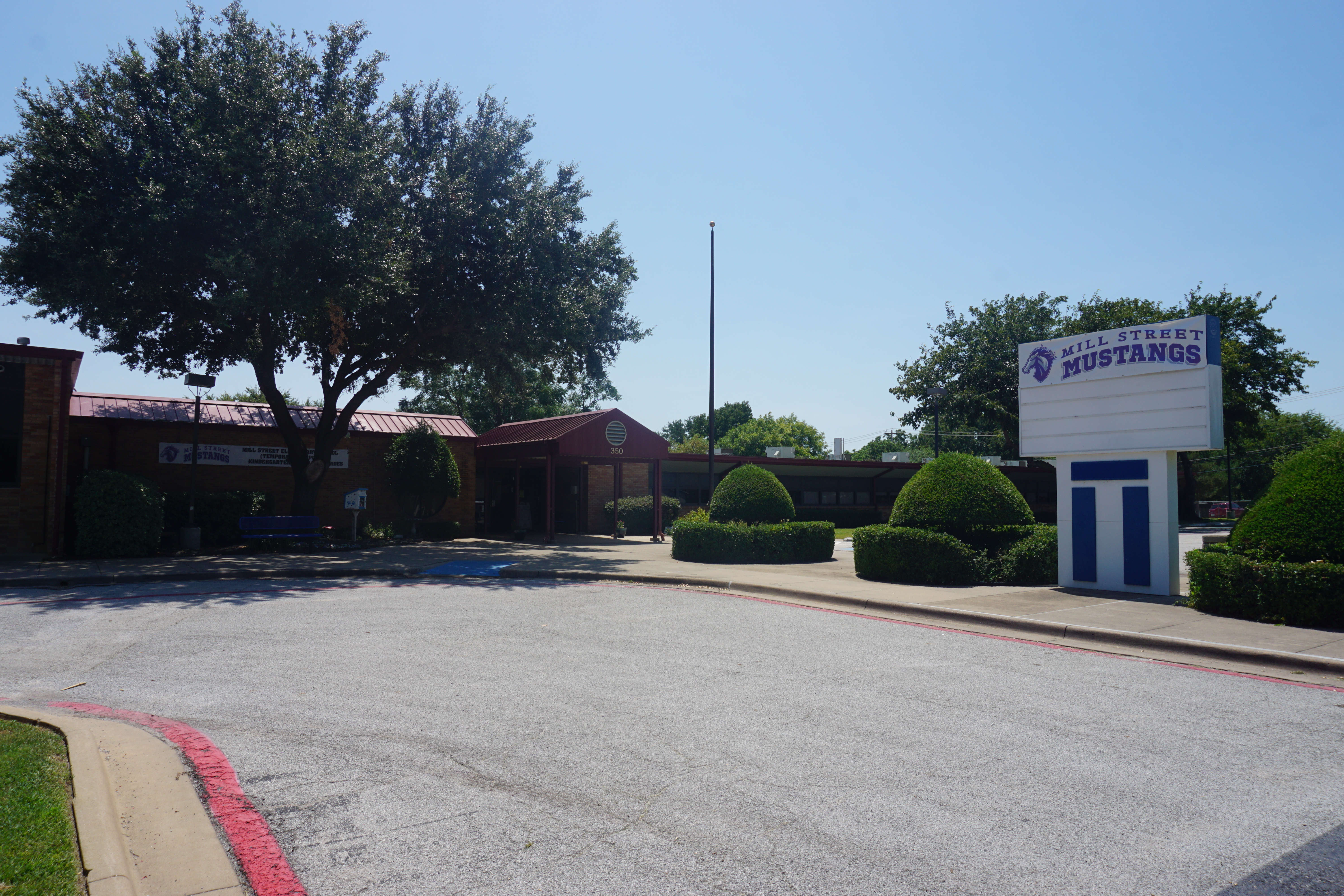 Single-story brick school building with a marquee sign reading 'Mill Street Mustangs' and trimmed hedges.