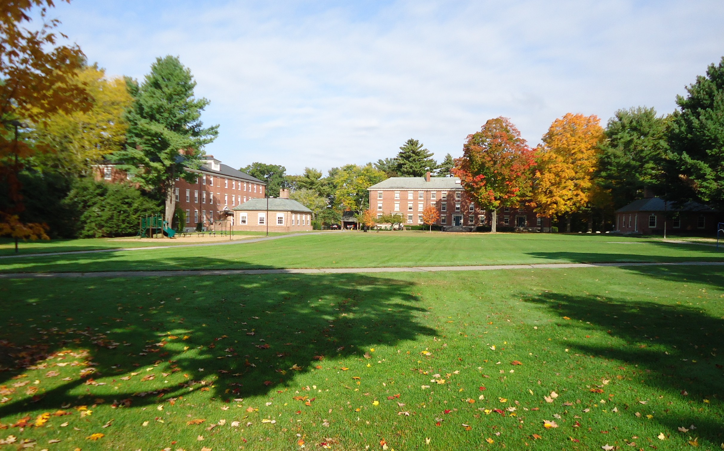 Wide green lawn flanked by brick buildings and autumn-colored trees on a boarding school campus.