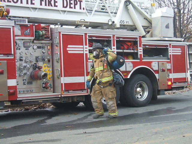 Firefighter in yellow bunker gear and SCBA mask walks beside a red ladder truck.