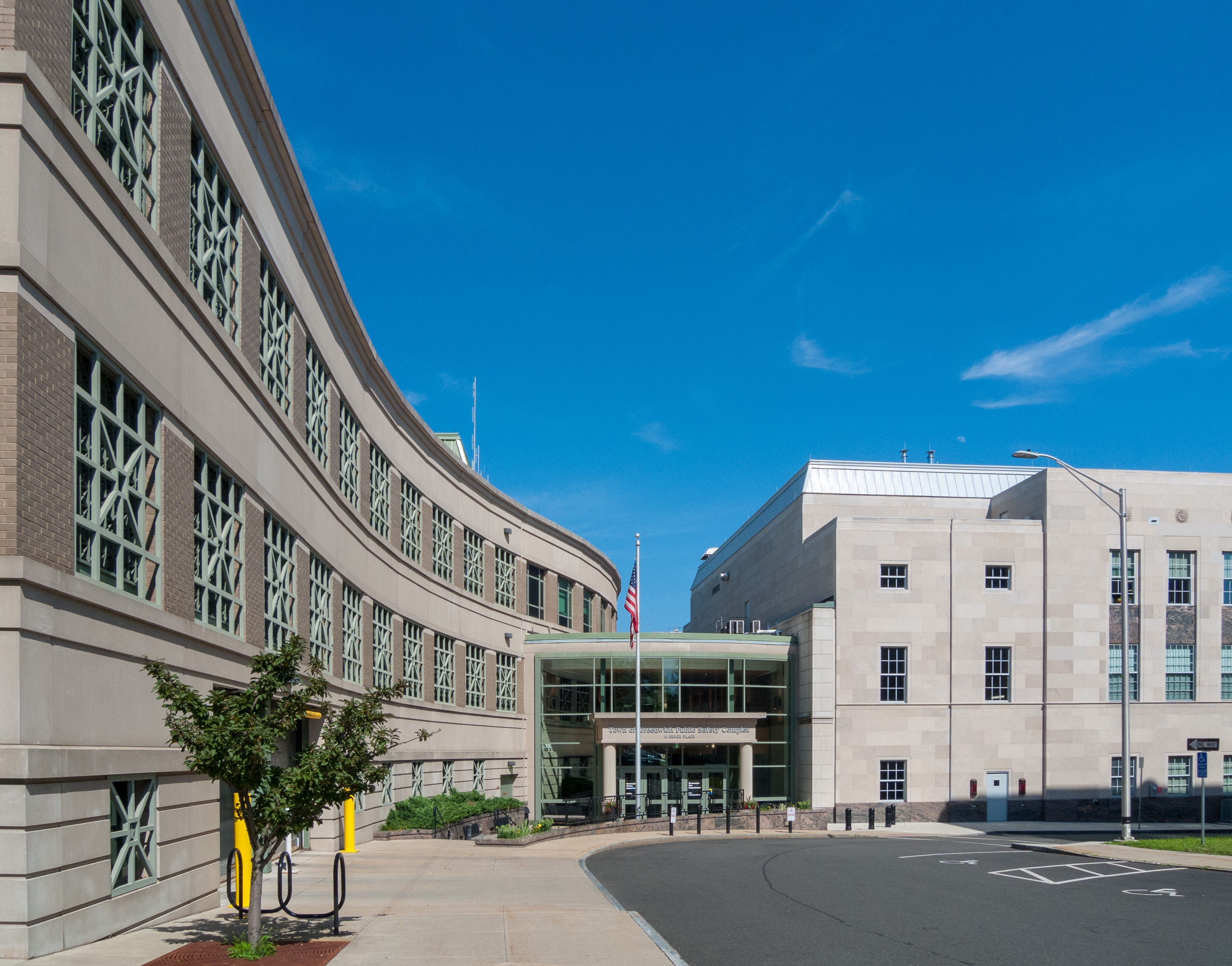Curved brick government building with green window grilles and an American flag at the entrance.
