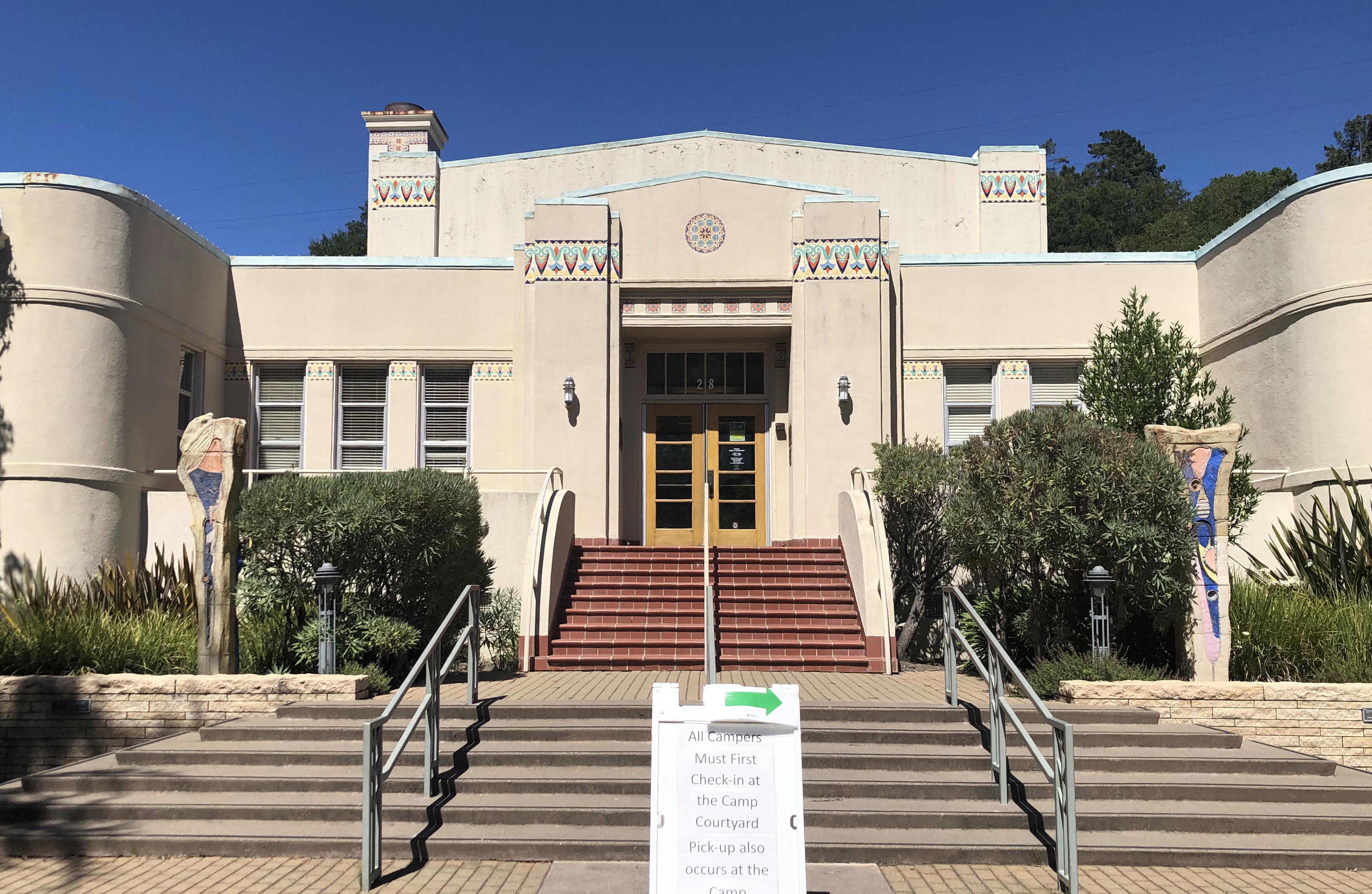 Art Deco civic building with red-brick steps and cylindrical towers under blue sky.