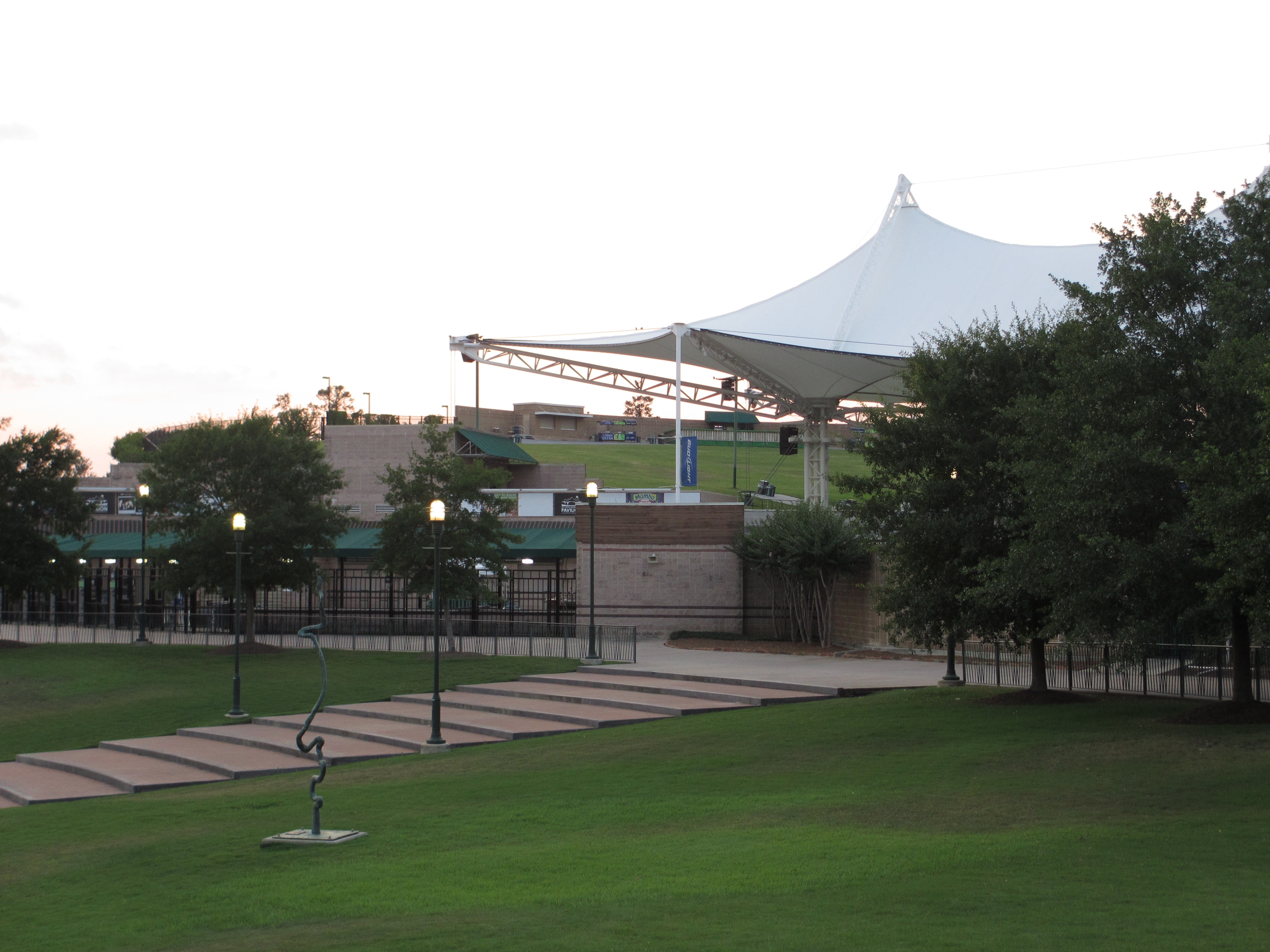 Outdoor amphitheater with a large white tensile canopy roof surrounded by trees and green lawn.