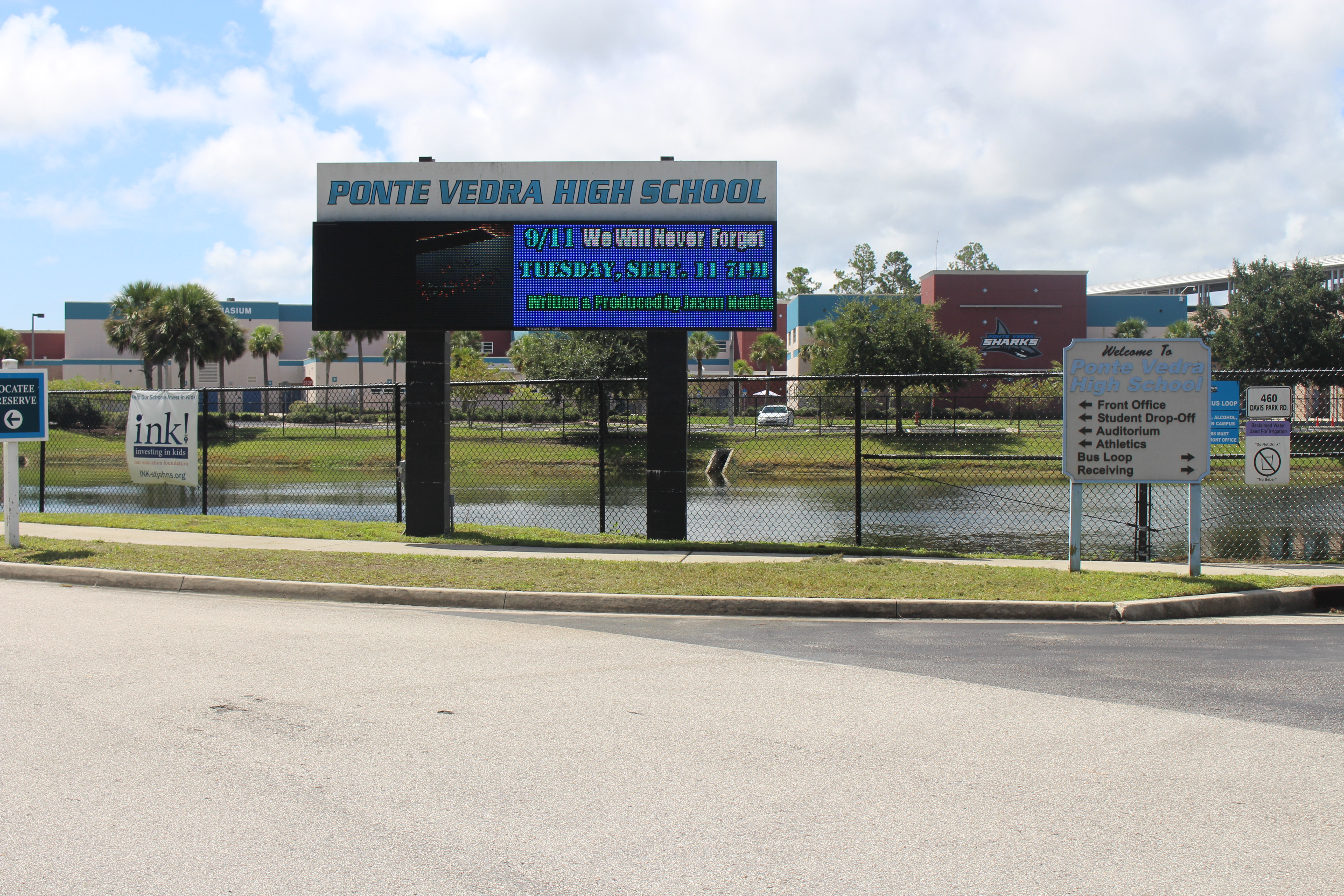 Exterior of a high school building with a marquee sign and retention pond.