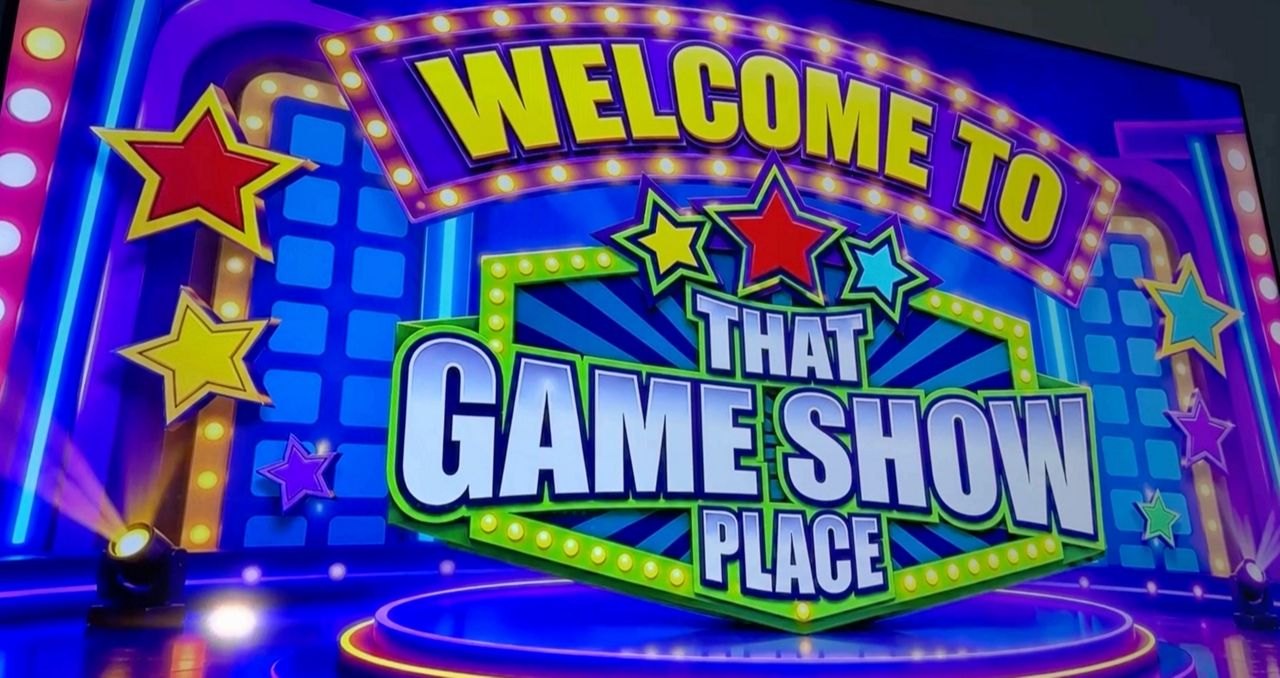 Colorful illuminated welcome sign with marquee lights and star graphics at a game-show venue.