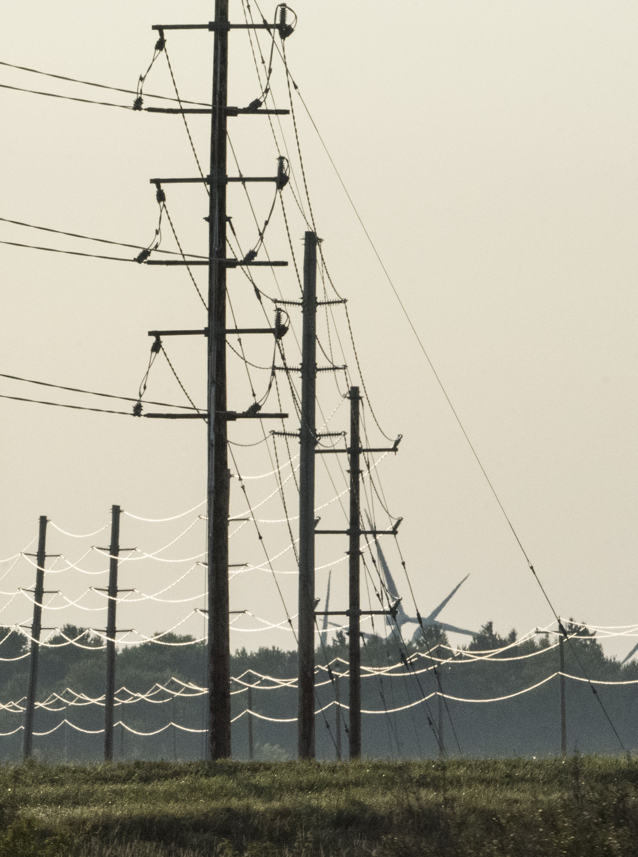 Wind turbines and power transmission lines along a rural highway under a cloudy sky.