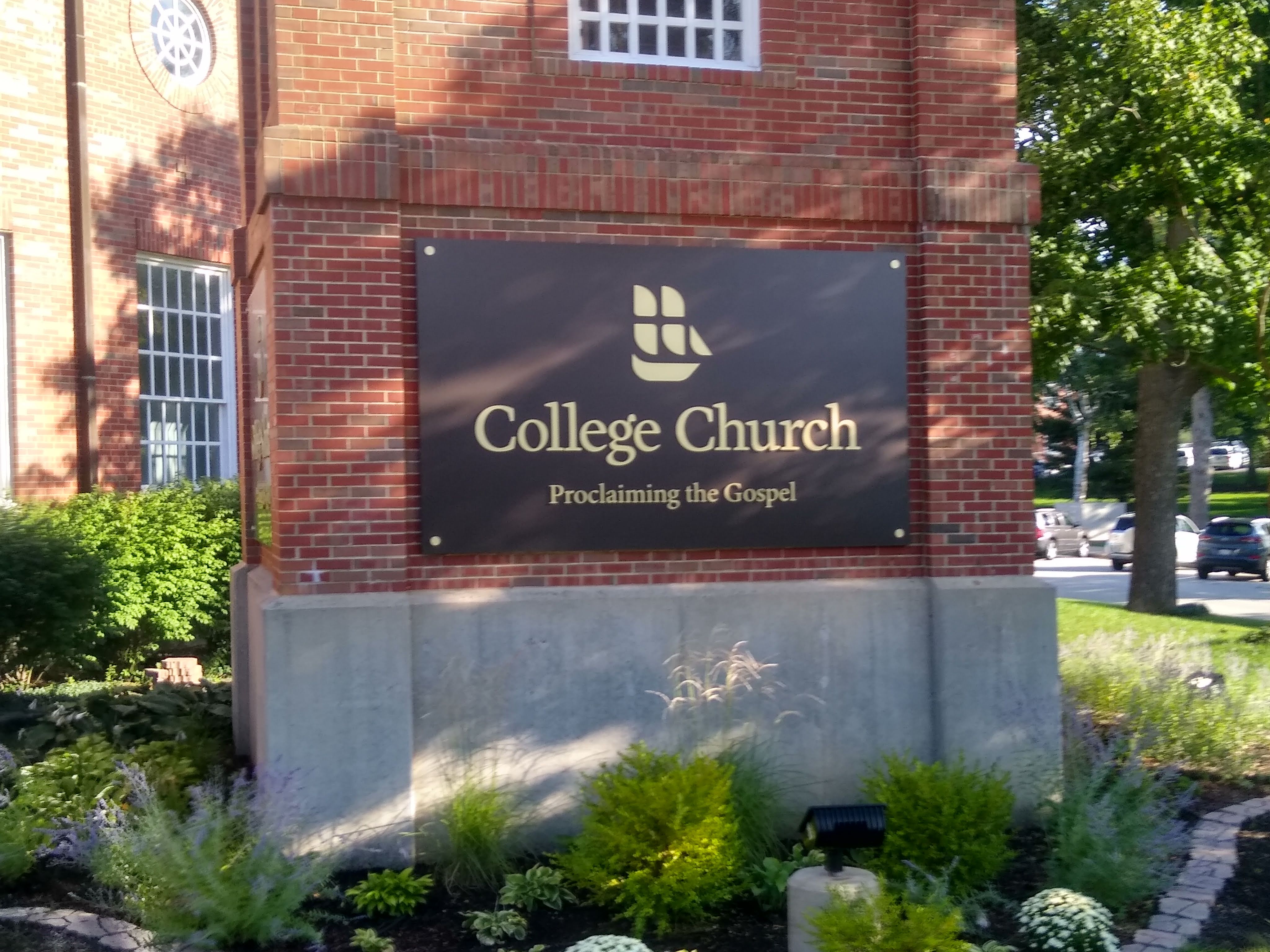 Sign reading 'College Church' mounted on a red brick building exterior with landscaping.