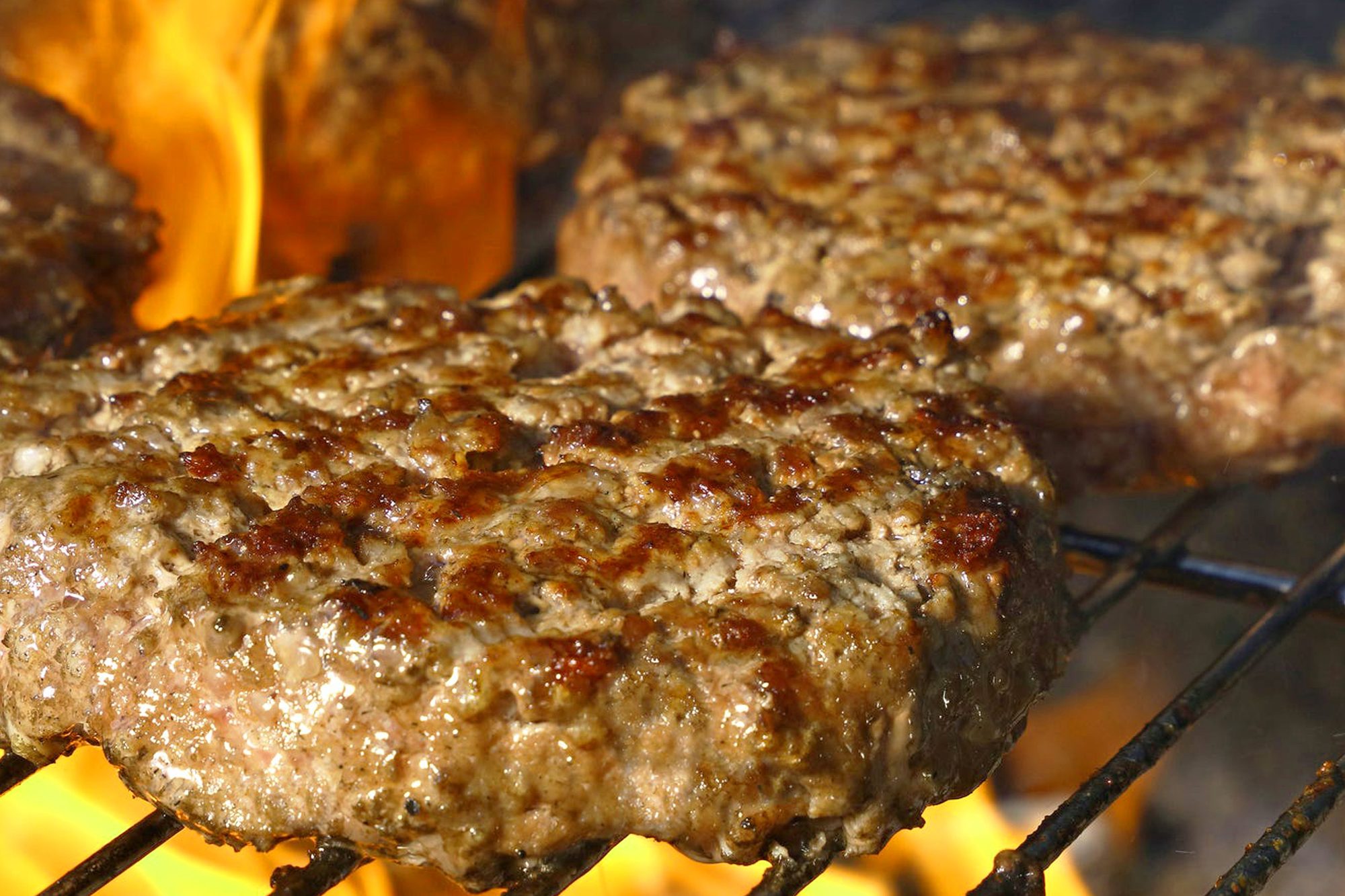 Close-up of juicy beef burgers grilling over open flames, perfect for summer BBQs.