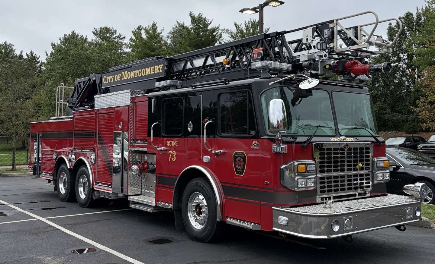 Red aerial ladder fire truck marked City of Montgomery, unit 73, parked in a lot.