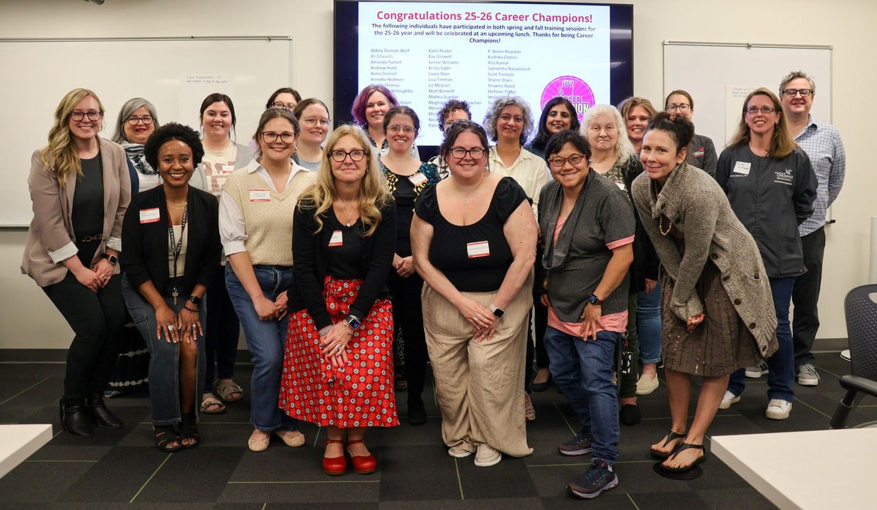Group of faculty and staff posing in a classroom in front of a congratulatory screen.