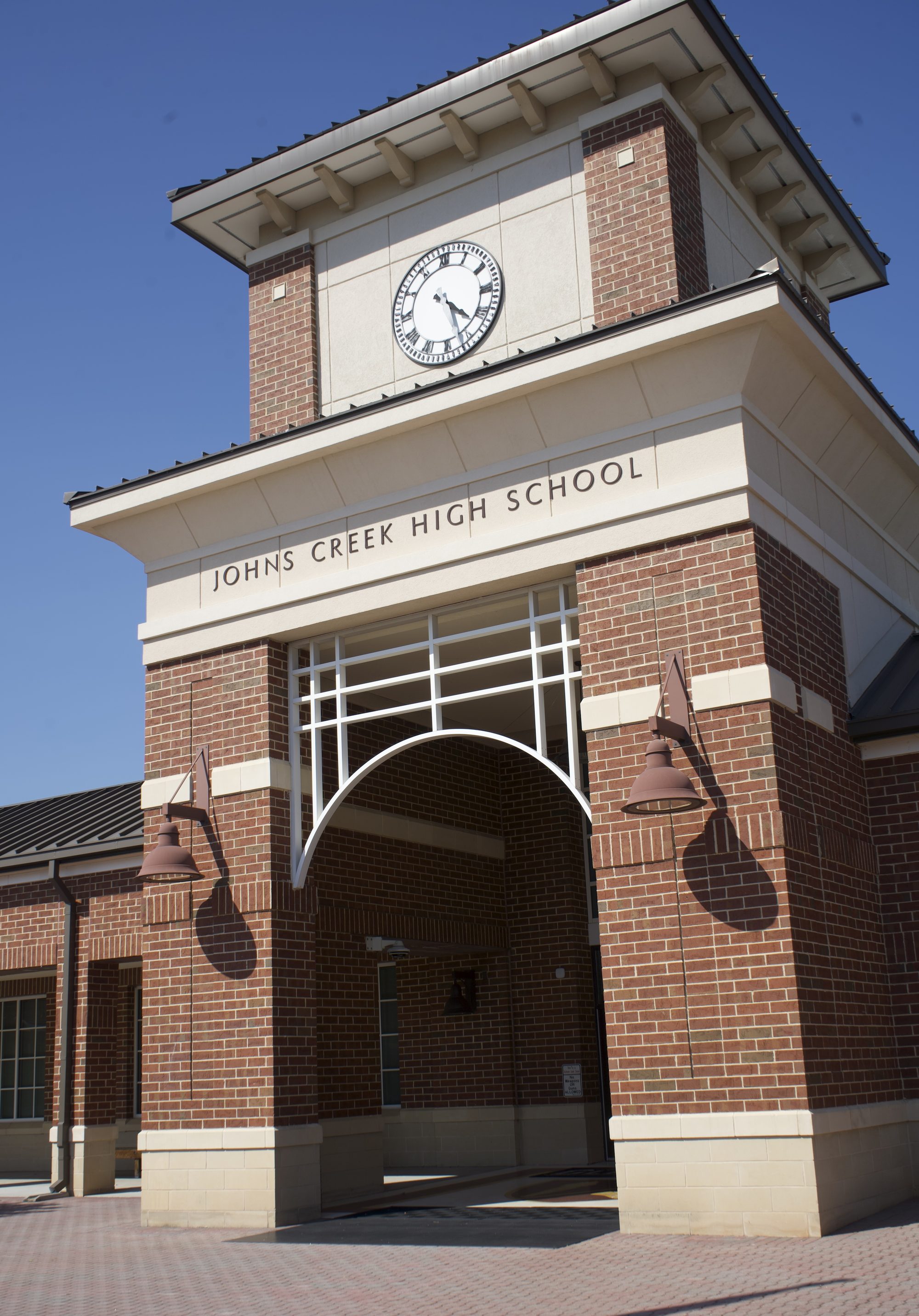 Brick entrance tower of a high school with an arched entryway and clock near the roofline.