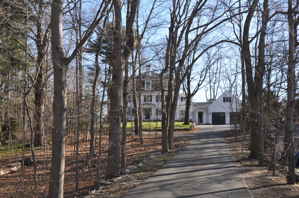 Tree-lined driveway leading to a large historic white house with a detached garage.