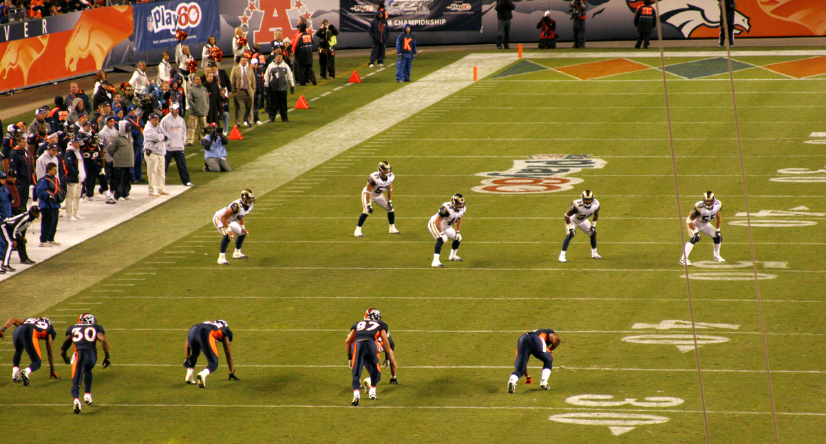 Denver Broncos players in orange and blue uniforms lined up on a football field.