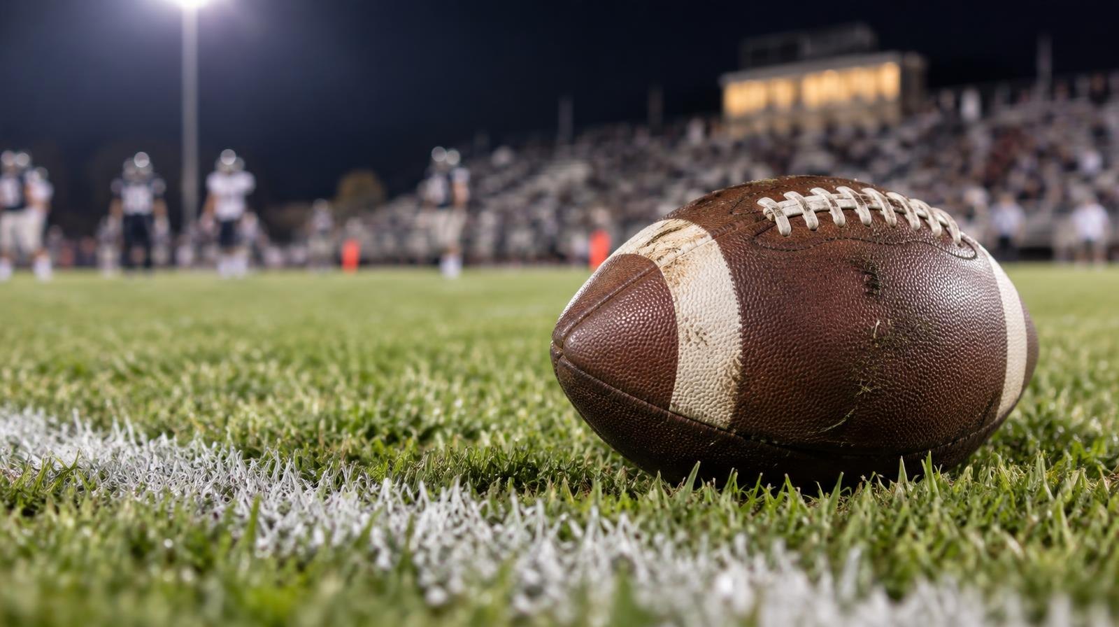 An American football resting on green grass beside a white painted yard line.