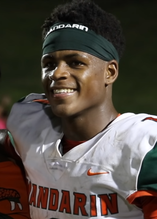 Football player in white Mandarin jersey and green headband at a nighttime game.