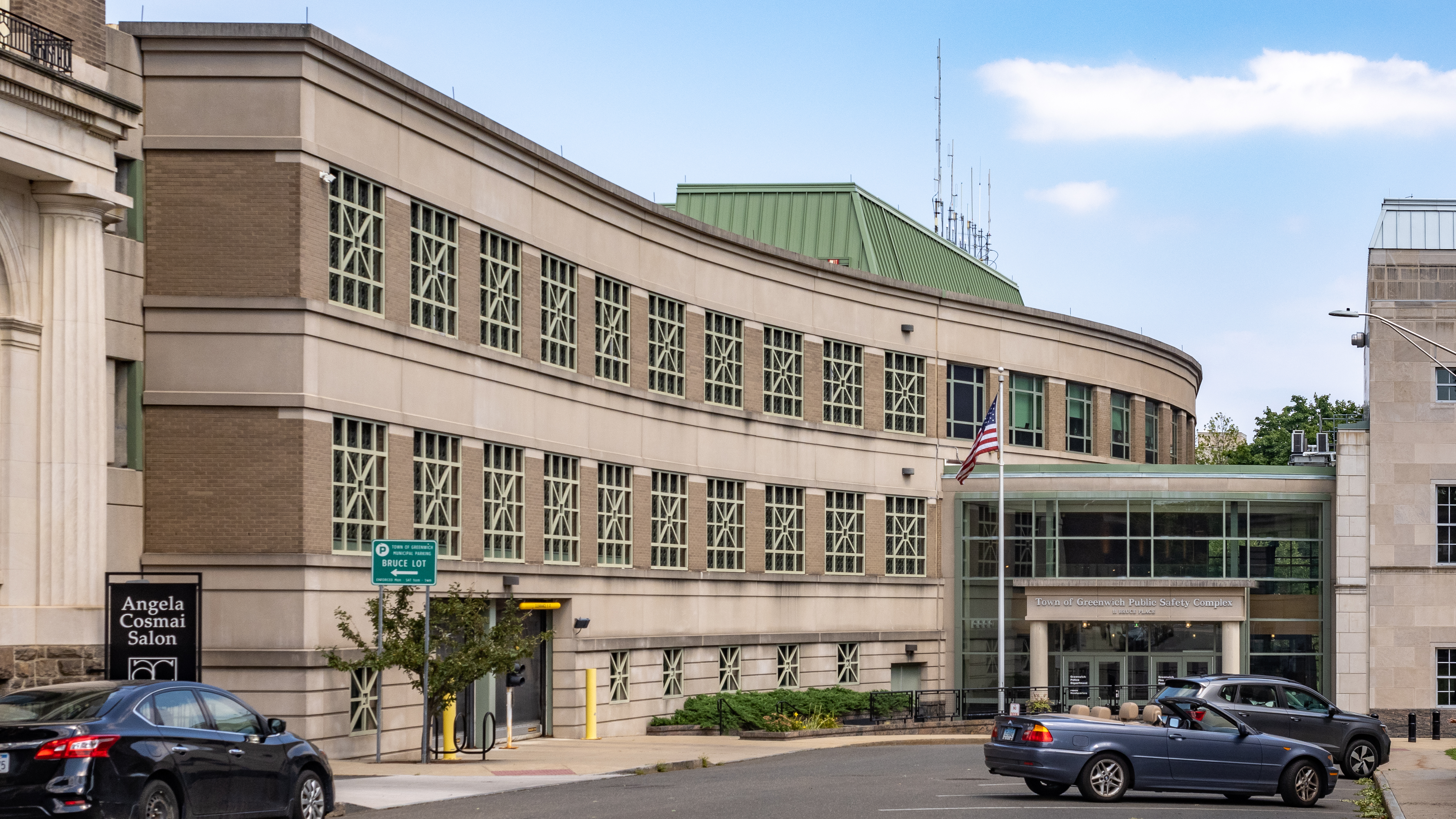 Two-story curved tan government building with green roof and American flag.