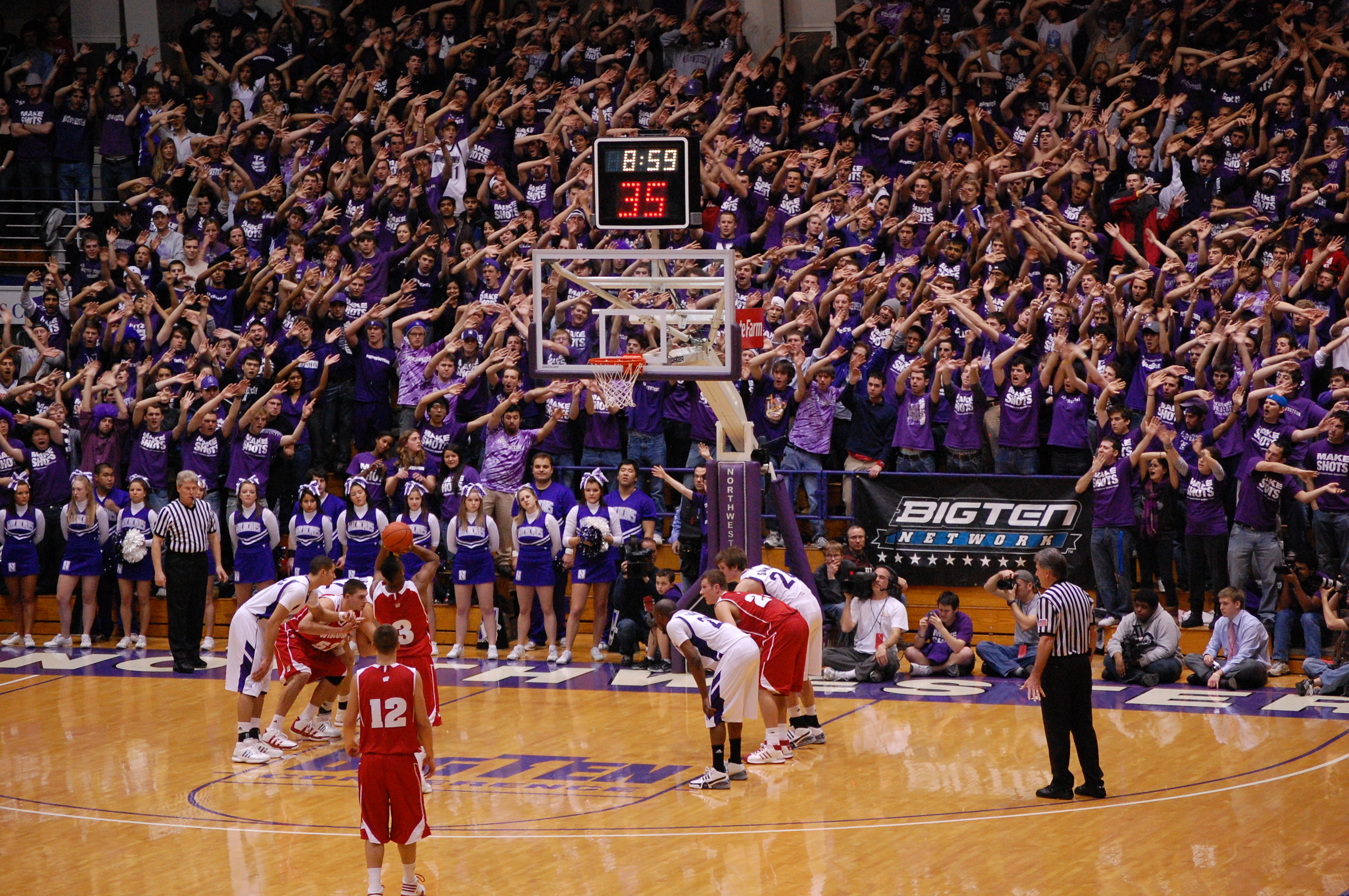 Basketball players compete on a hardwood court before a packed arena crowd.