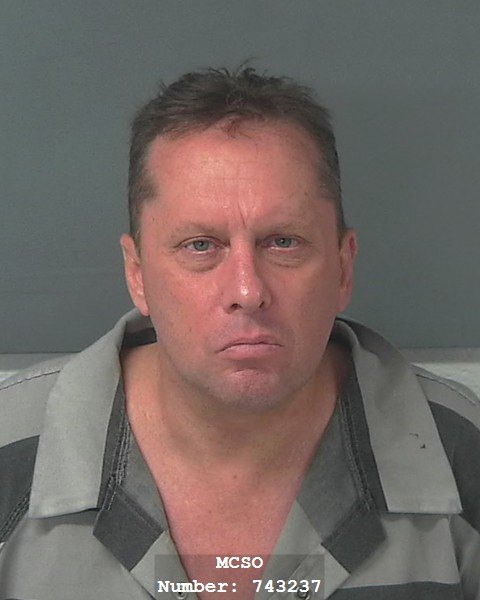 Booking photo of a man in a gray striped jail uniform against a gray background.