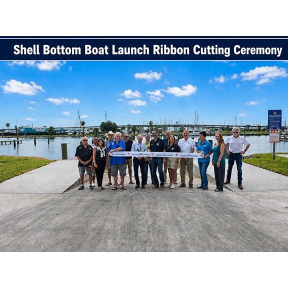 Group of people holding a ribbon on a concrete boat ramp at a waterfront marina.