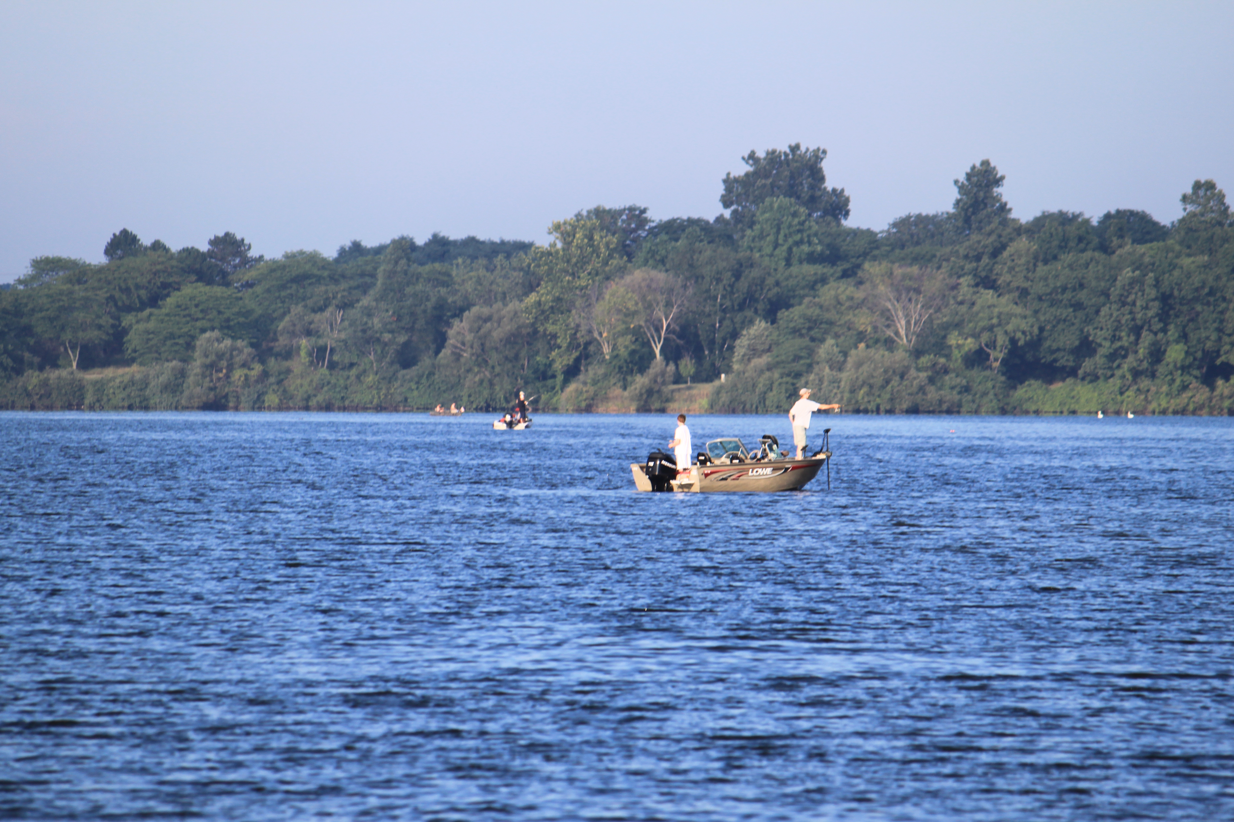 Two small motorboats with anglers fishing on a calm, tree-lined lake.