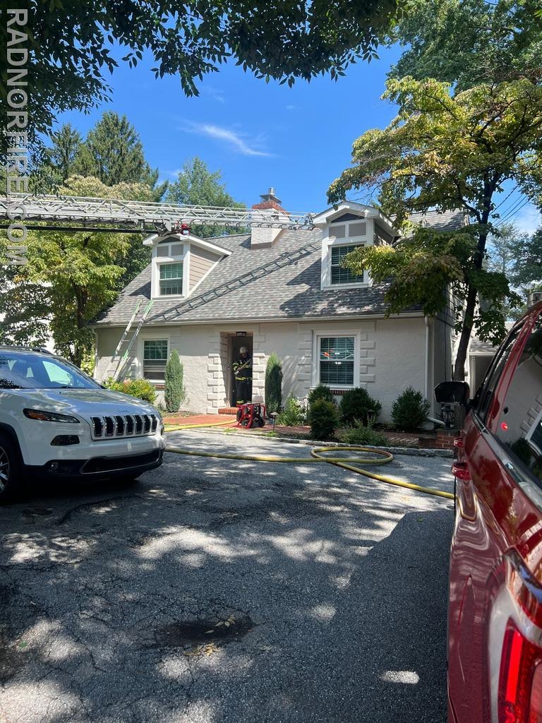 Aerial ladder raised to roof of two-story home with fire hoses stretched across driveway.