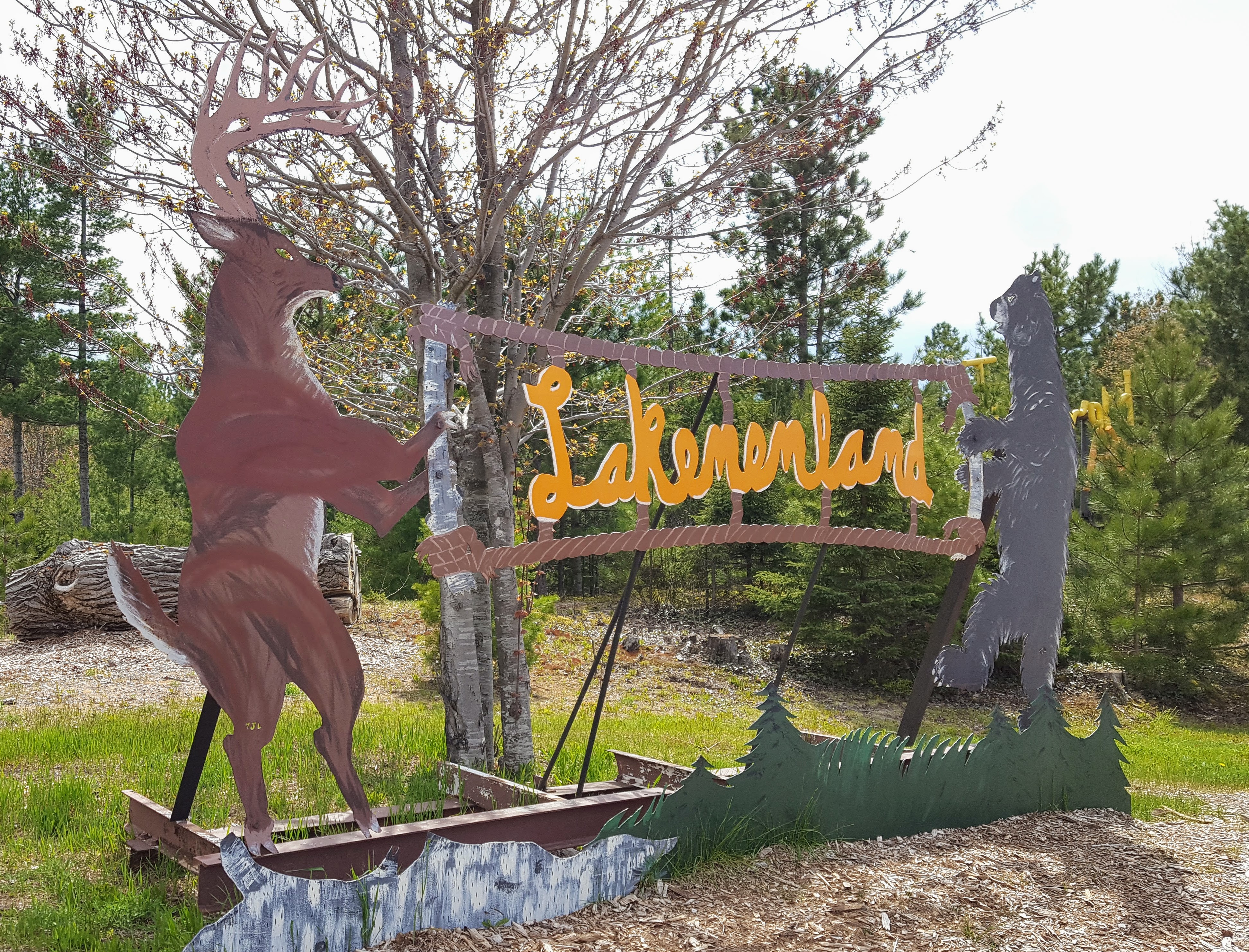 Scrap metal deer and bear sculptures holding a sign at the entrance to an outdoor sculpture park.