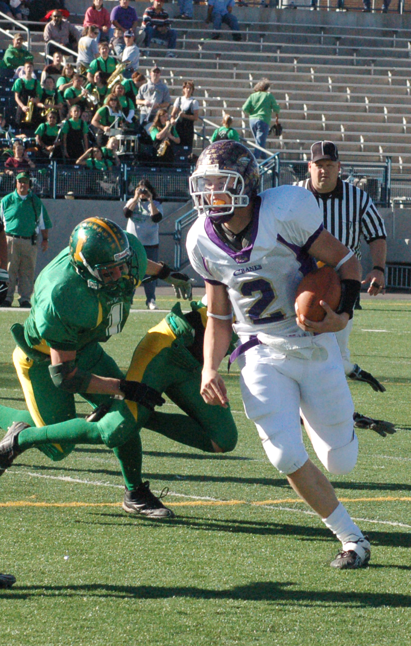 A football player in a white uniform runs with the ball past a defender.