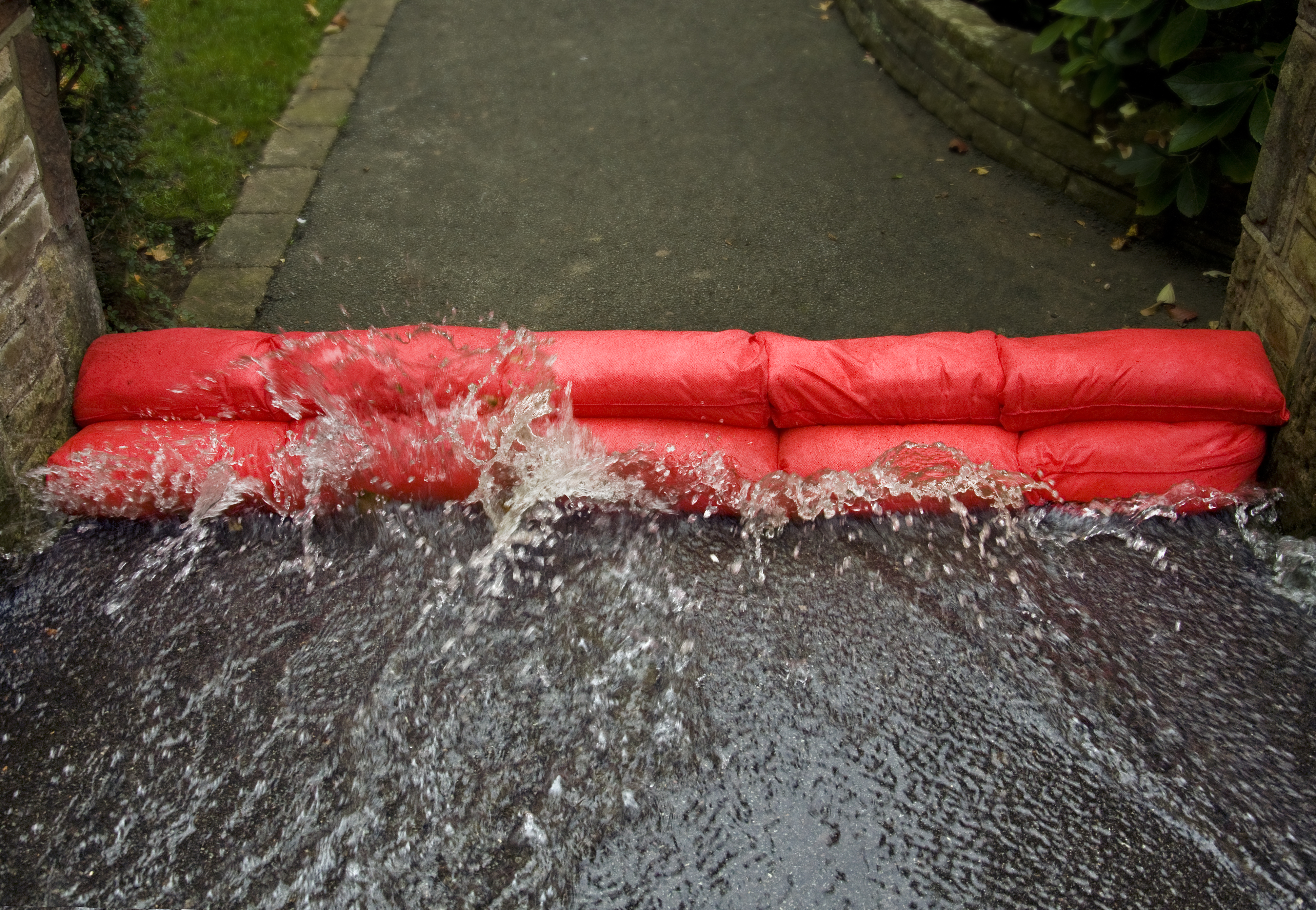 Red sandbags in a line across a driveway with water splashing over them.