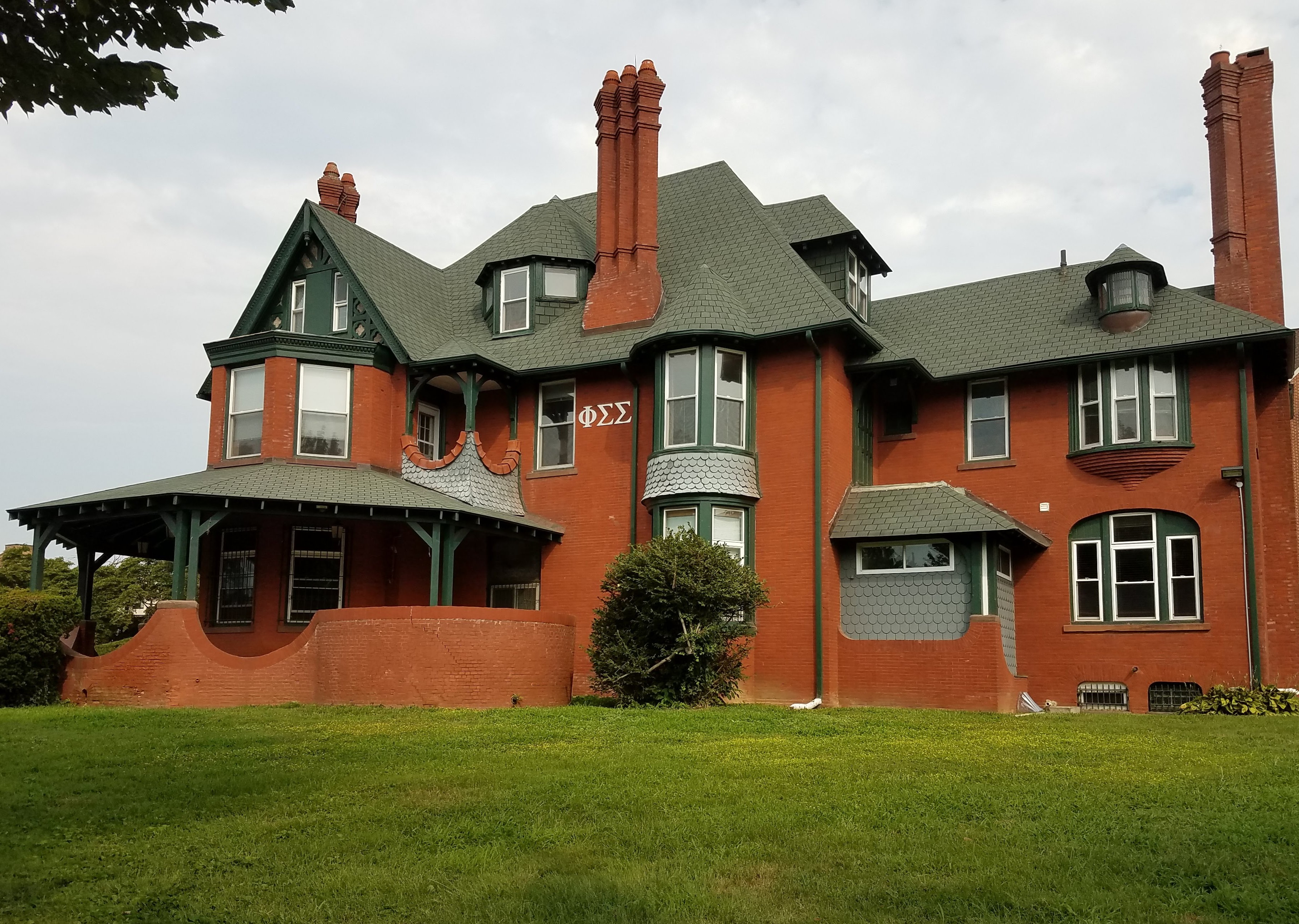 Victorian red brick manor house with green trim and wraparound porch on a university campus