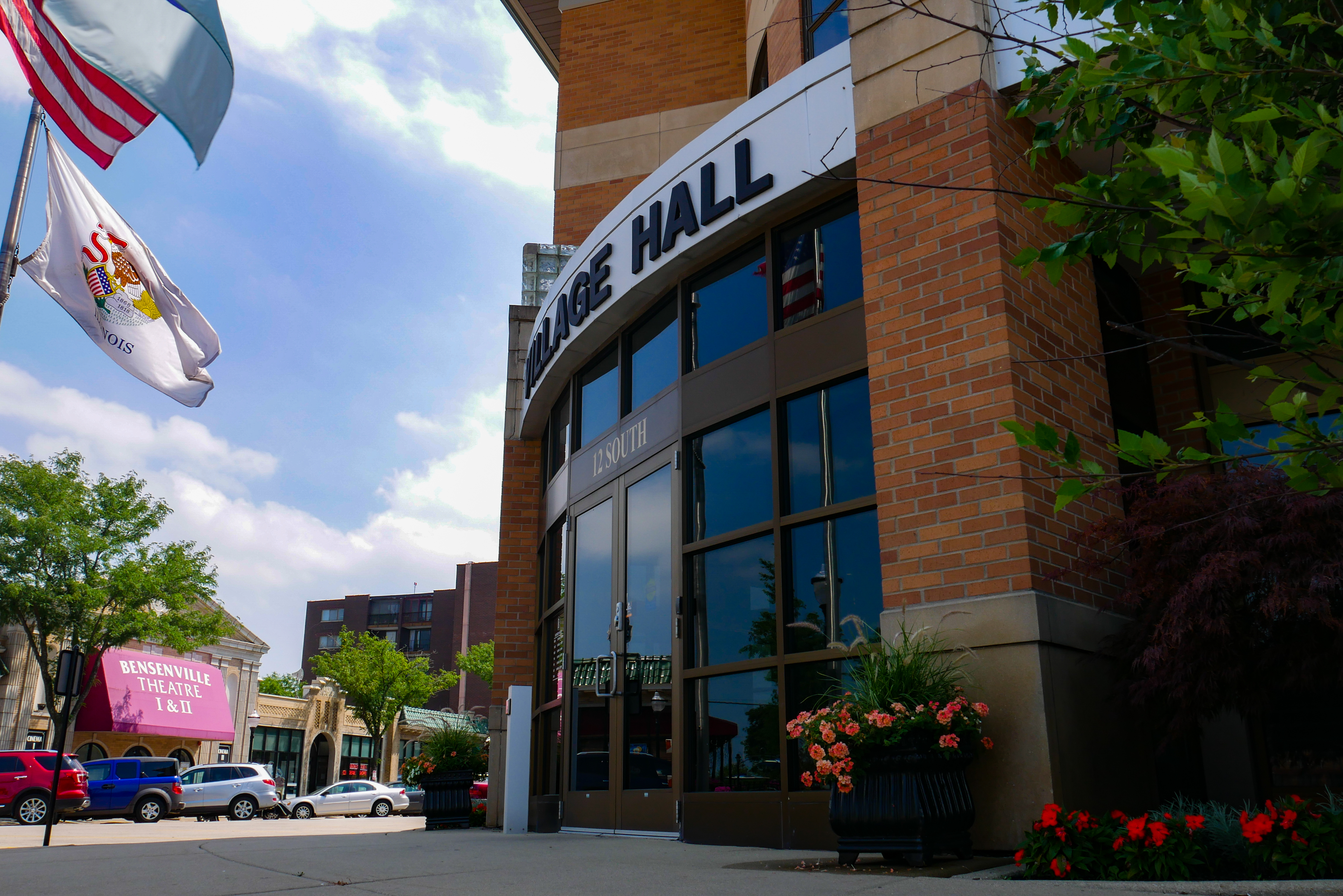 Brick village hall building with glass entrance doors and American and Illinois flags outside.