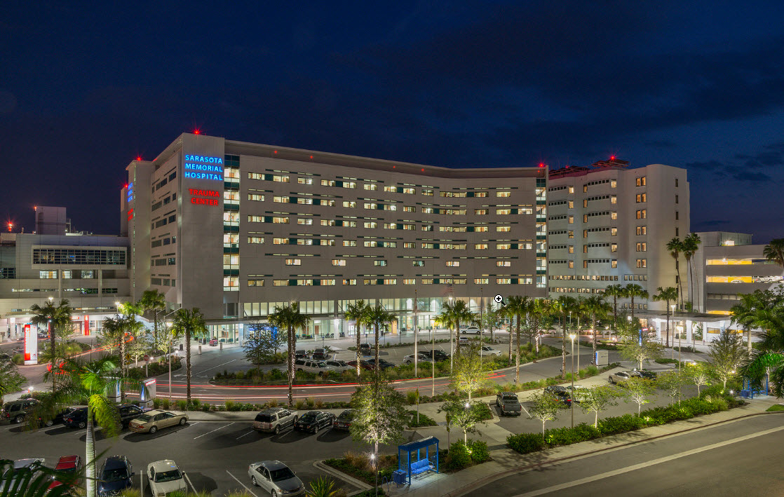 Large multi-story hospital building illuminated at night with palm trees in front.