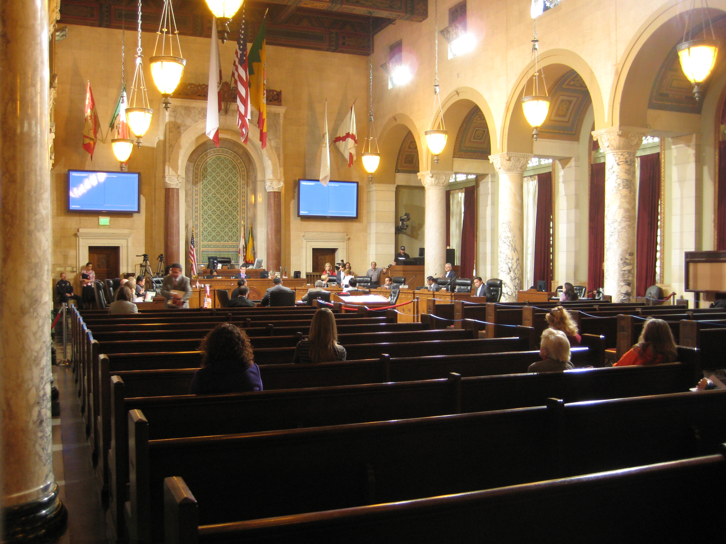 Interior of a formal city council chamber with wooden pews and a raised dais.