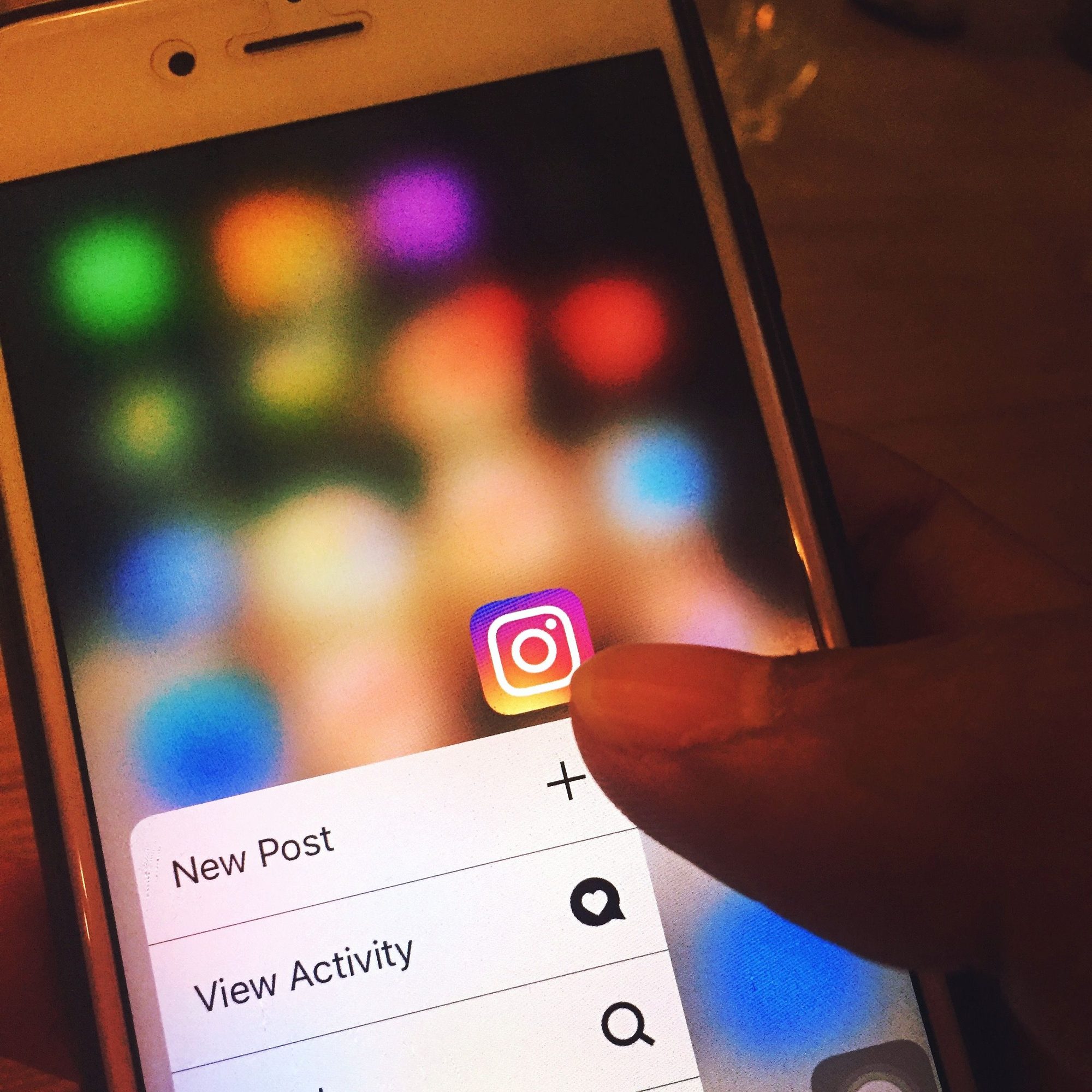 Finger navigating Instagram app on a smartphone screen with colorful blurred background.