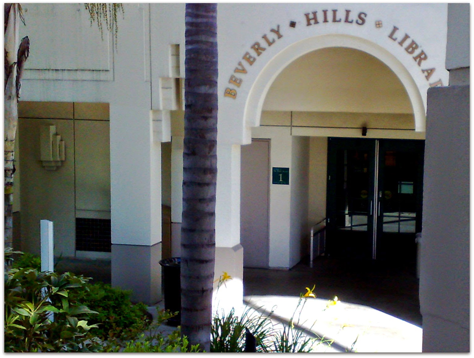 Arched entrance to the Beverly Hills Public Library with palm tree and landscaping in the foreground.