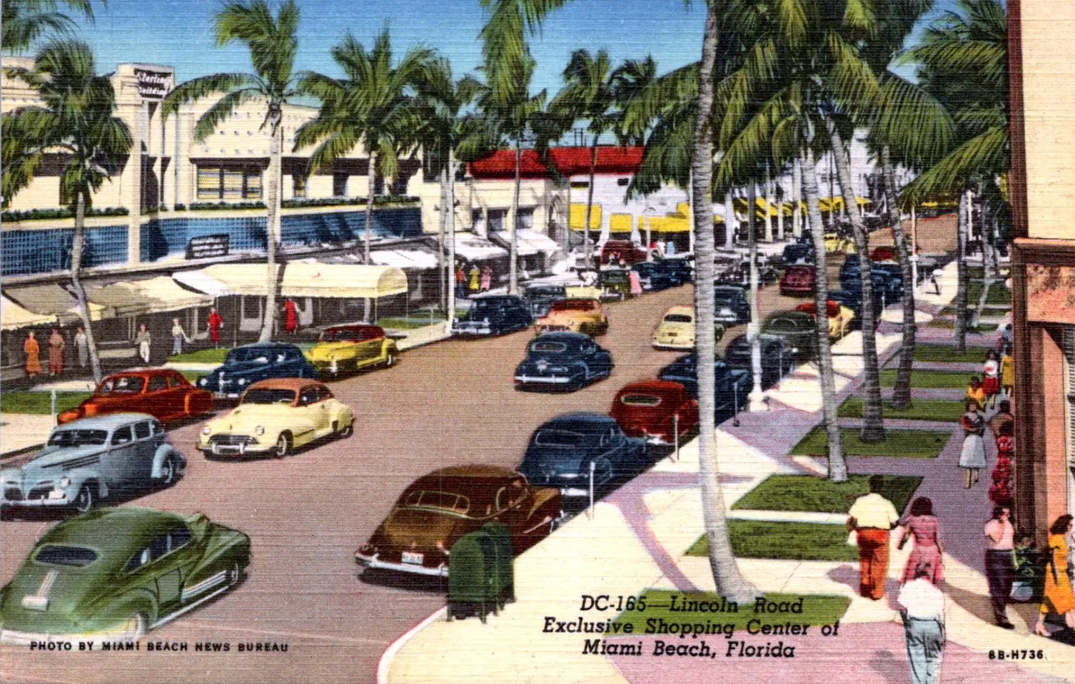 Colorized 1940s postcard showing a busy palm-lined shopping street with period automobiles and storefronts.
