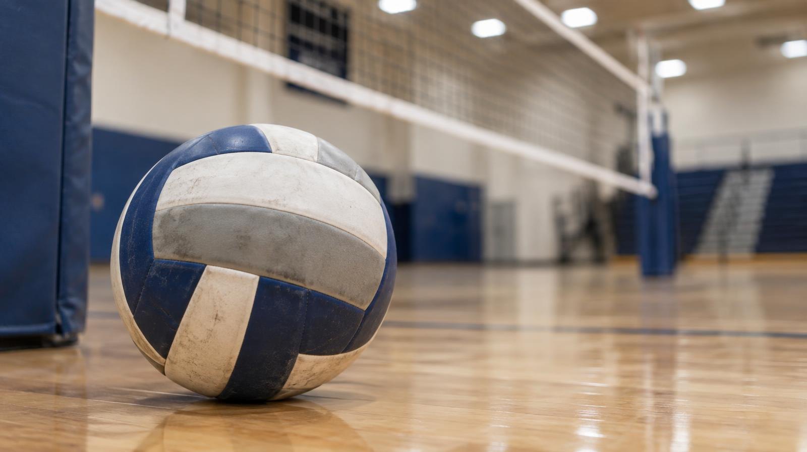 A volleyball resting on a hardwood gymnasium floor near the net post.
