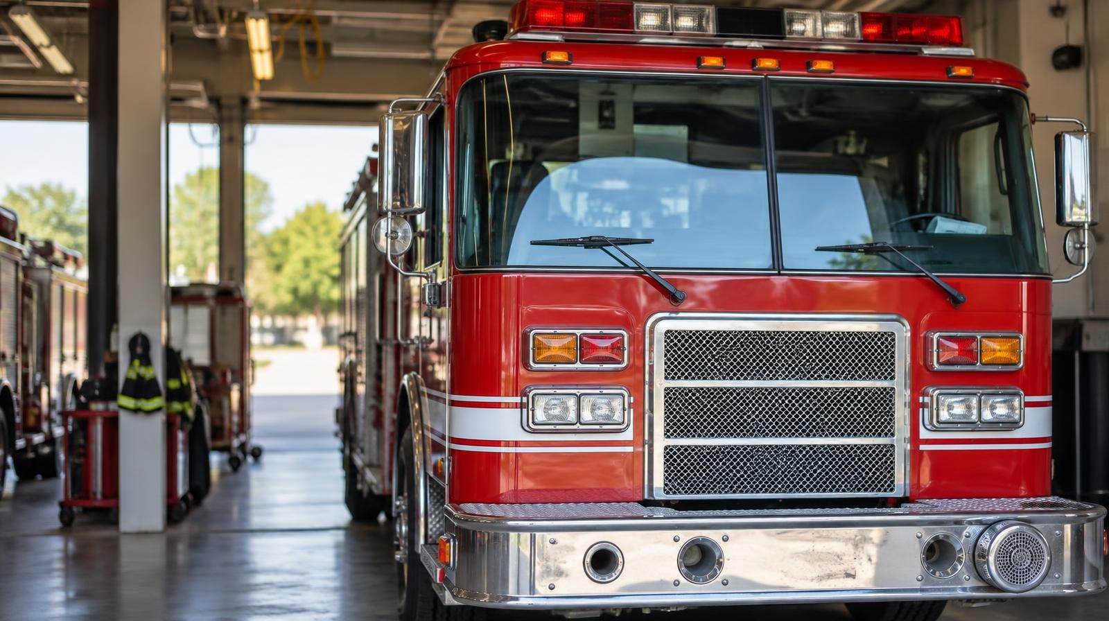 A red fire engine parked inside a bright modern fire station bay with open doors.