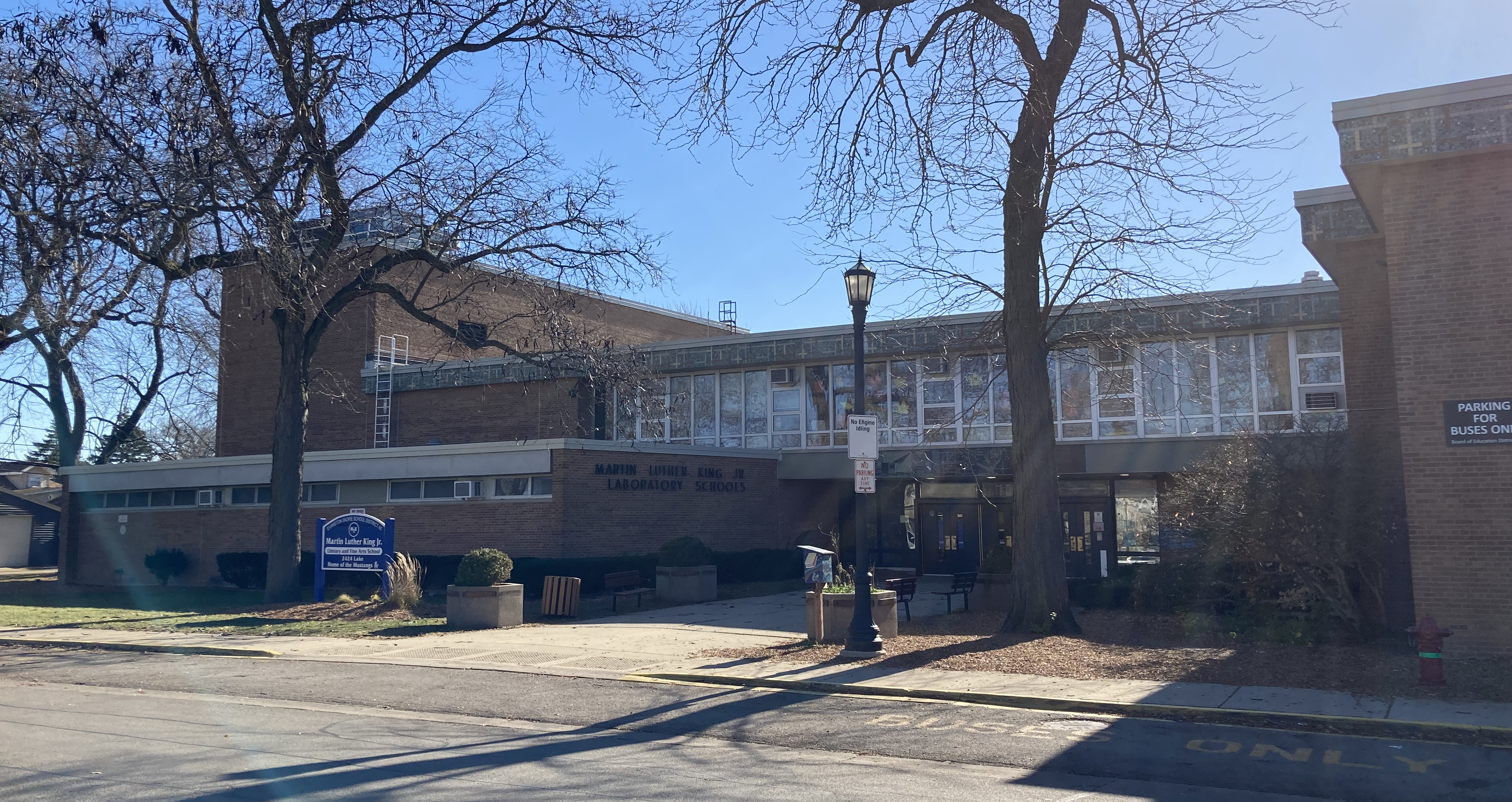Two-story brick school building with large windows and a blue entrance sign.