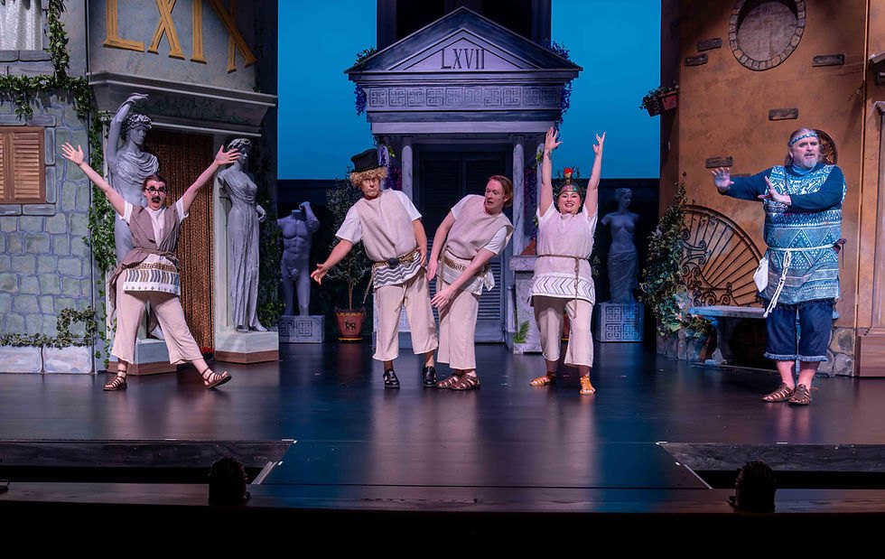 Five performers in ancient Greek costumes on a colorfully lit theatrical stage.