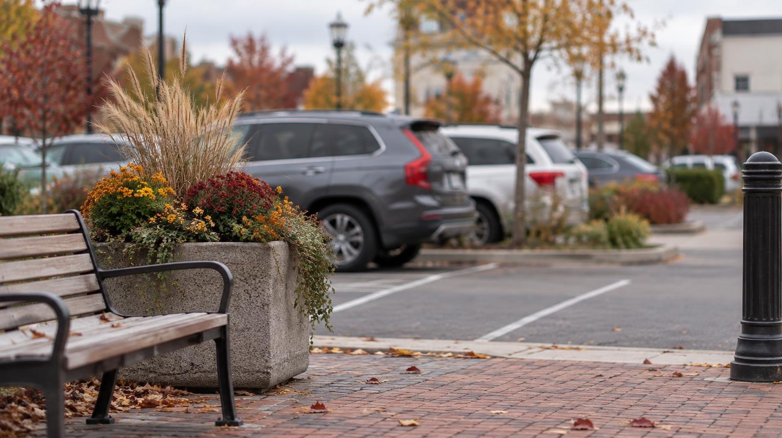 A surface parking lot with painted white lines next to a small urban plaza with benches.