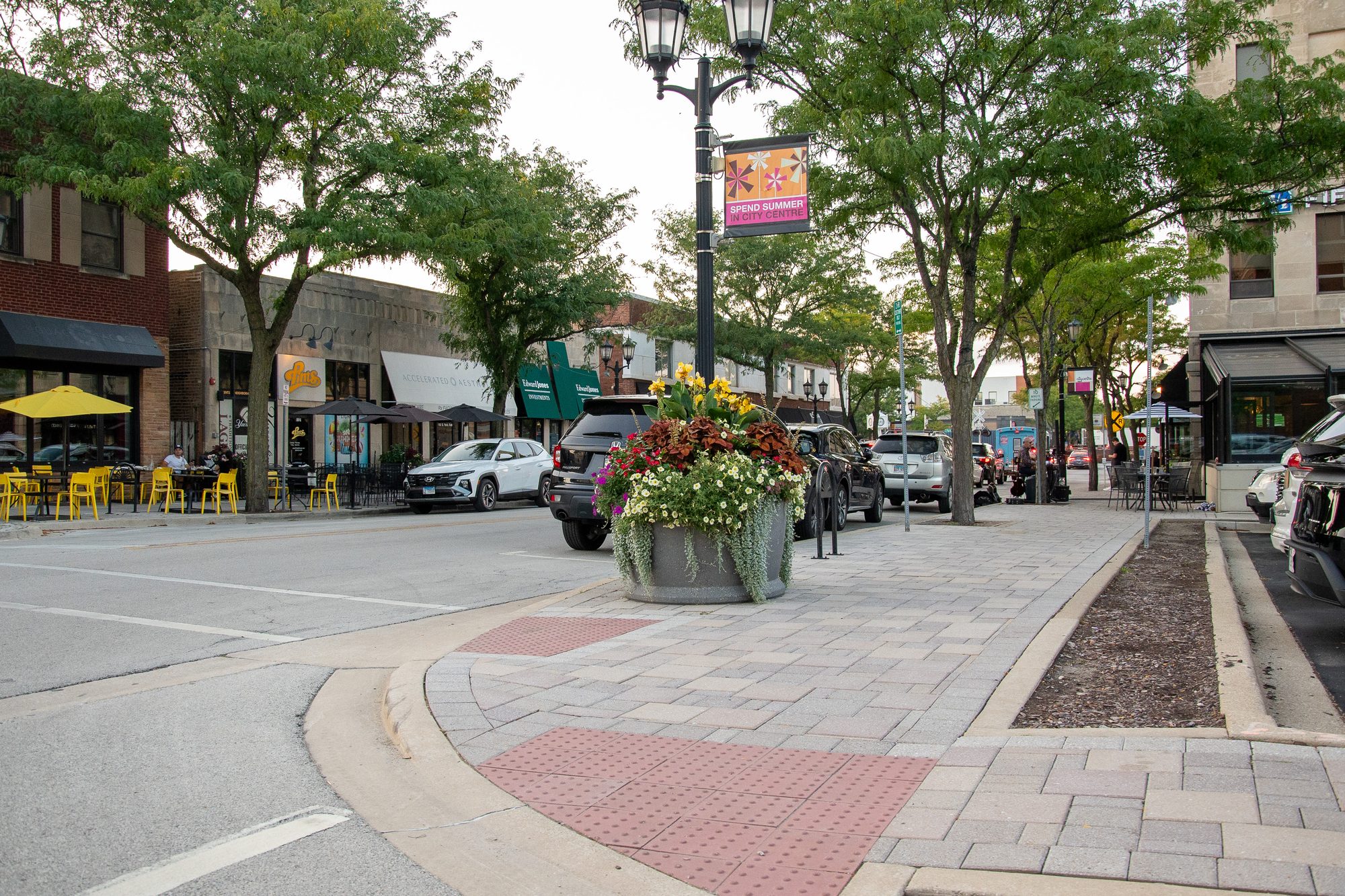 Brick-paved downtown street with flower planter, street lamp, and retail storefronts.
