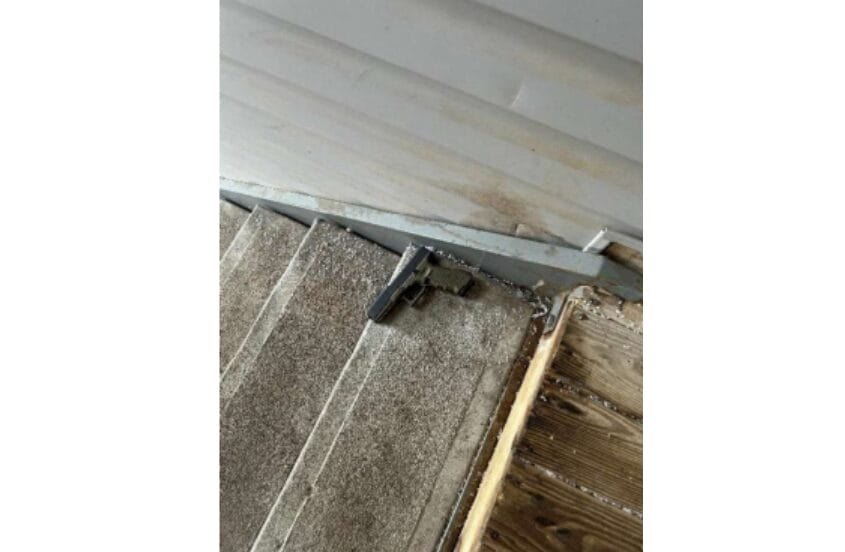 A black handgun lying on carpeted stairs near a metal door threshold.
