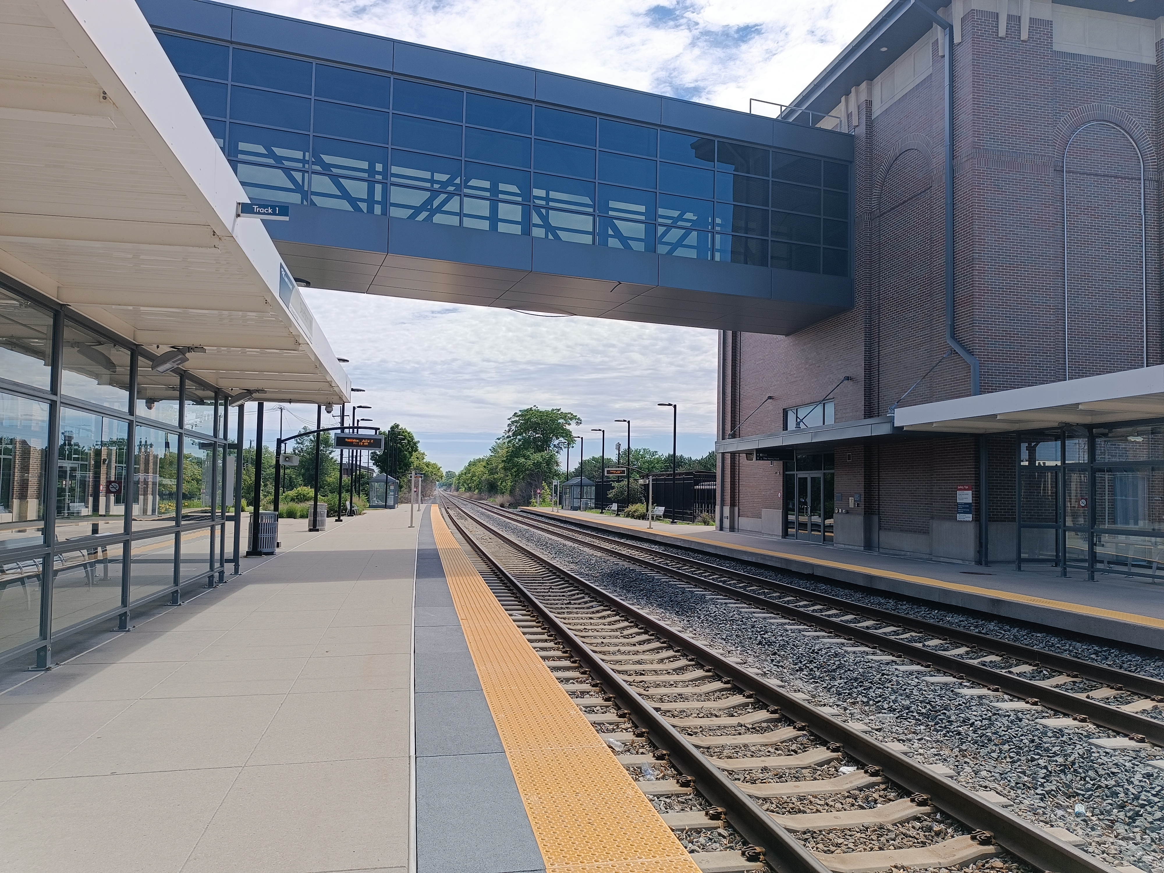 A commuter rail platform with two sets of tracks and a glass pedestrian bridge spanning overhead.