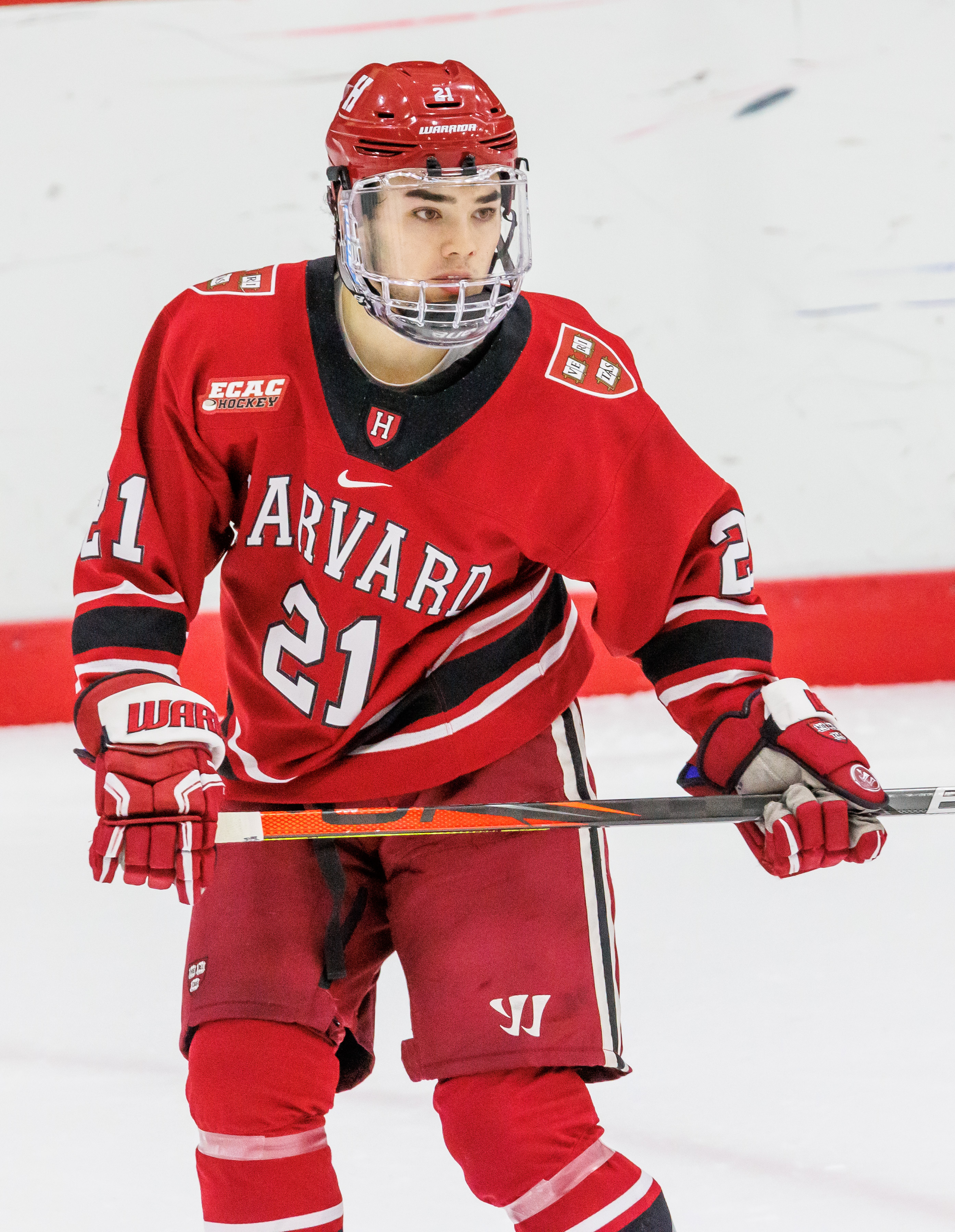 Hockey player in a red Harvard Crimson jersey skating on the ice.