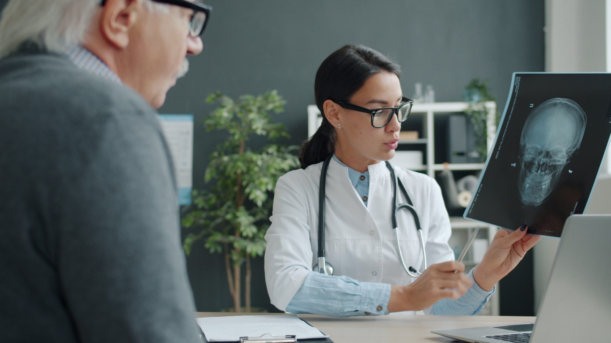 A female doctor discussing a brain X-ray with an elderly patient in a modern medical office setting.