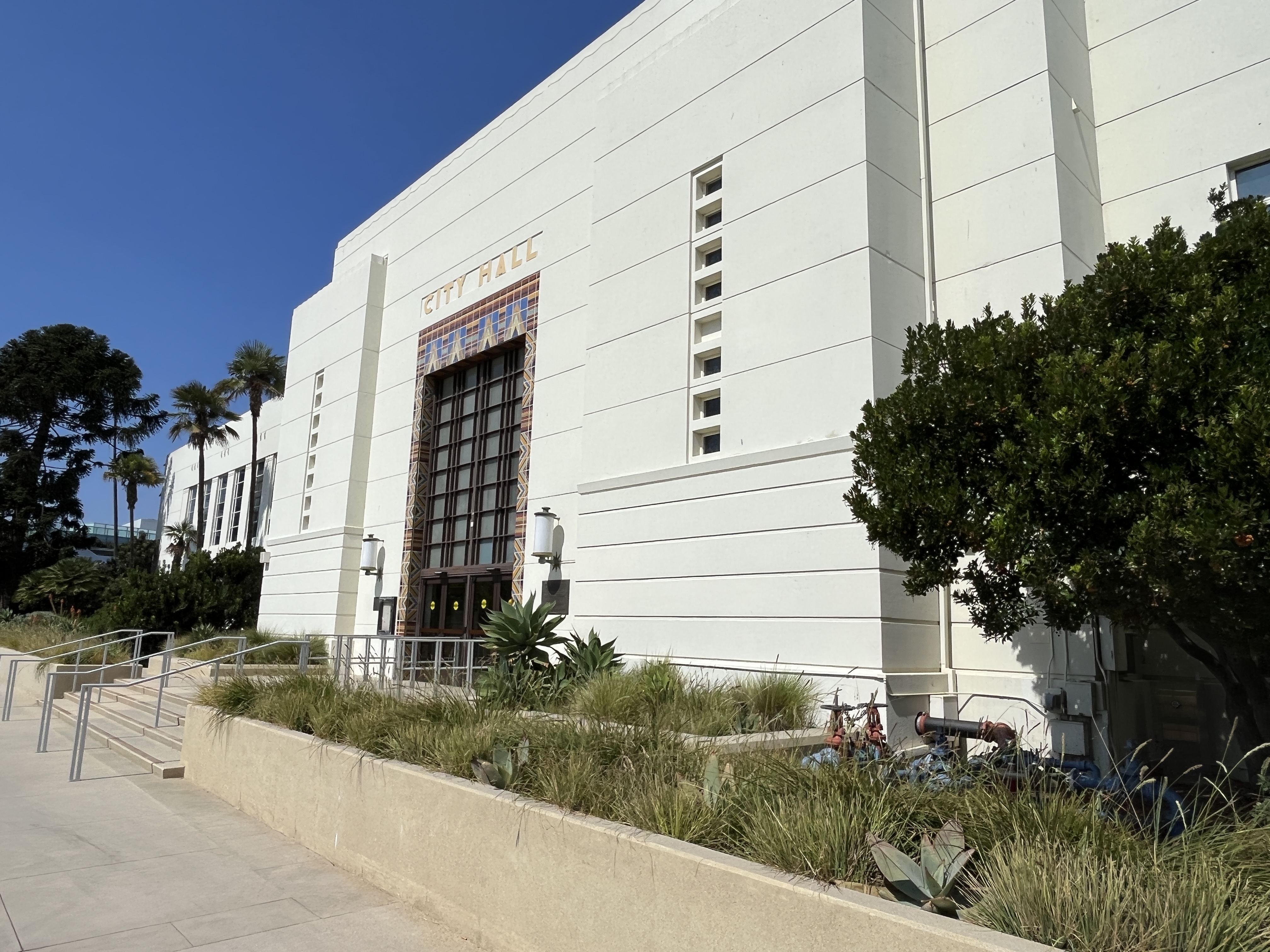 White Art Deco city hall building with palm trees and bicycle racks out front.