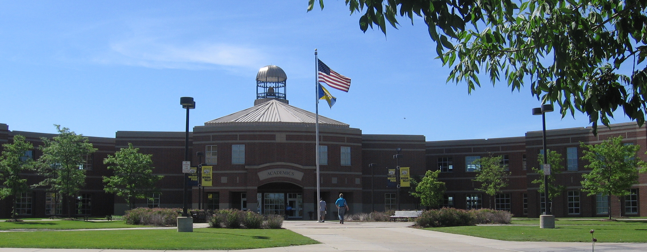 Brick high school building with domed entrance tower and American flag on a sunny day.
