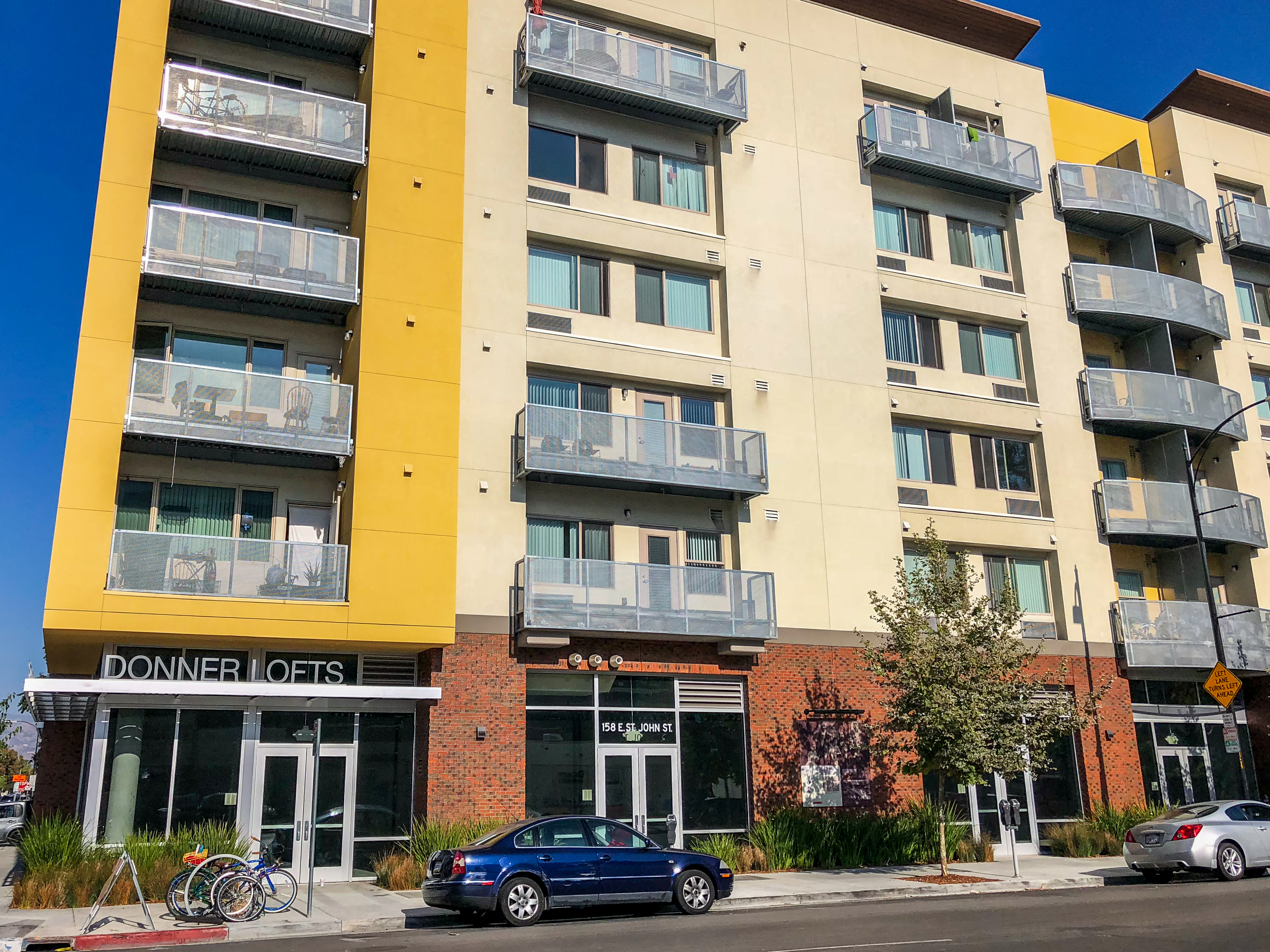 Six-story affordable housing apartment building with yellow facade and street-level retail.