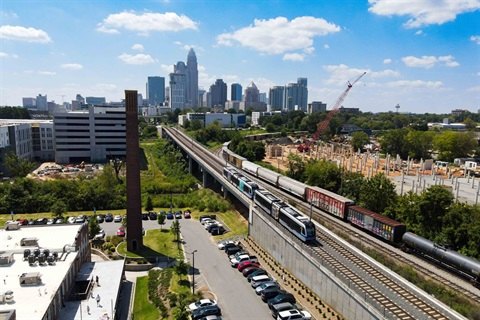 A light-rail train on an elevated track with a city skyline behind it.